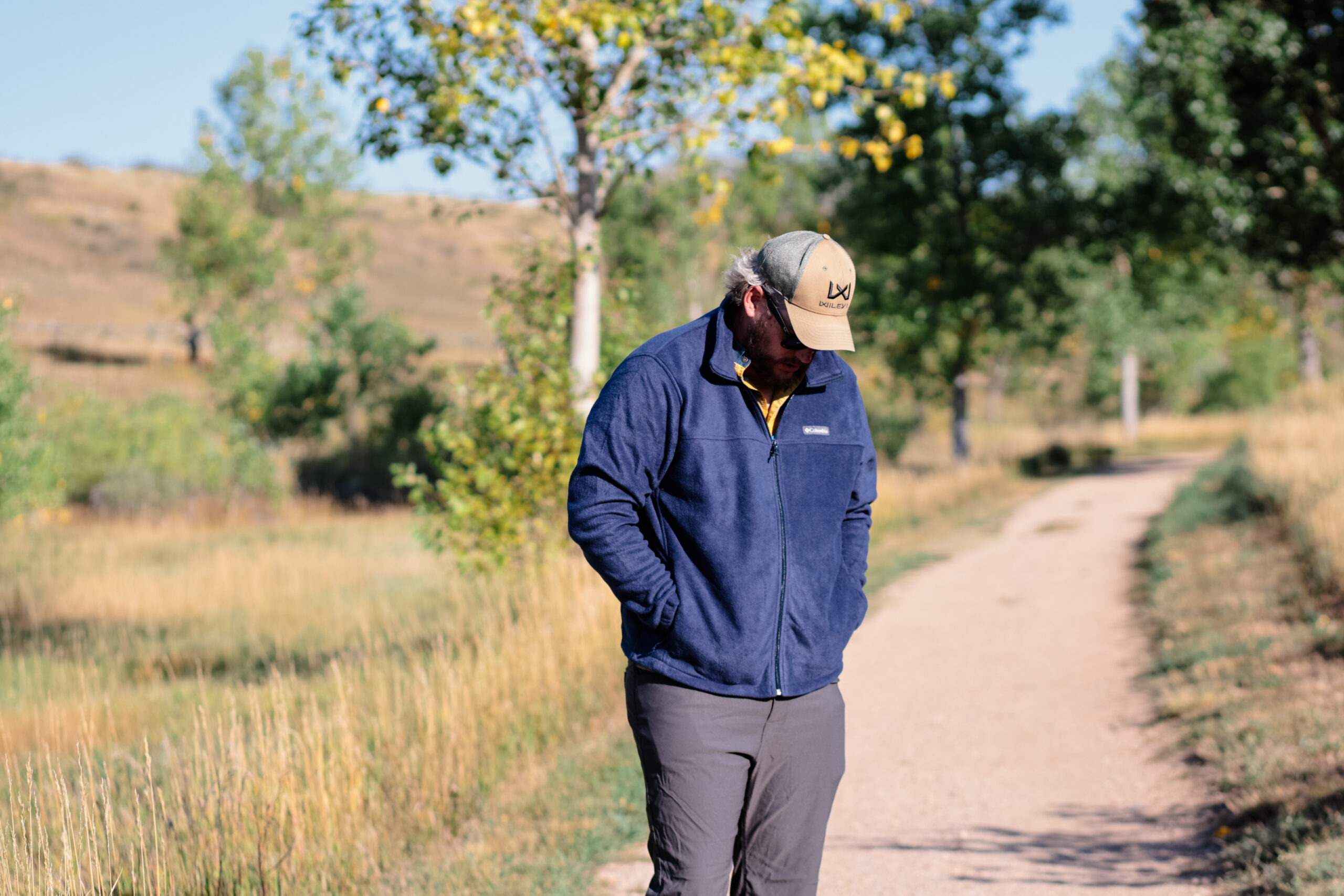 A man wearing a blue fleece looks down while walking on a trail.