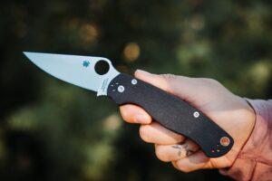 Holding the Spyderco Para Military 2 pocket knife in the open position with an outdoor background