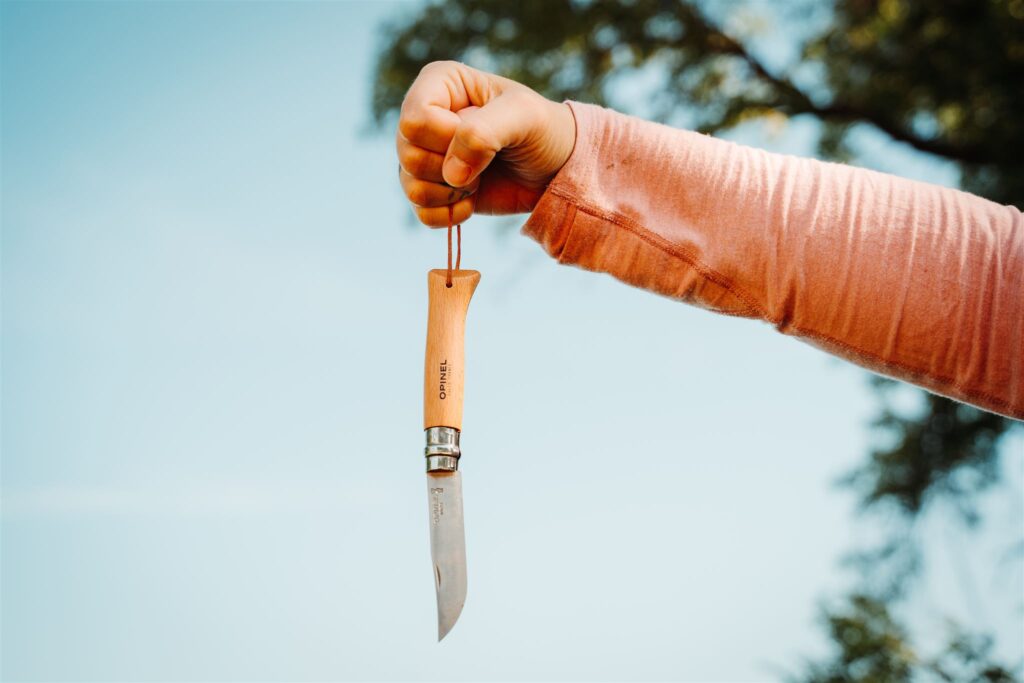 The Opinel No. 8 pocket knife being held up by the handle loop with an outdoor background.