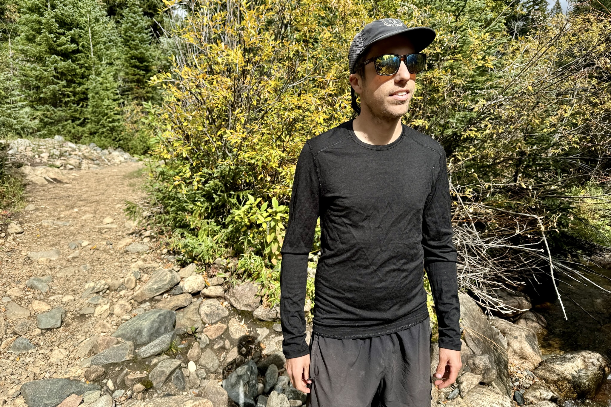 A hiker stands on a trail wearing the Icebreaker Oasis 200 base layer. Trees and a trail are in the background.