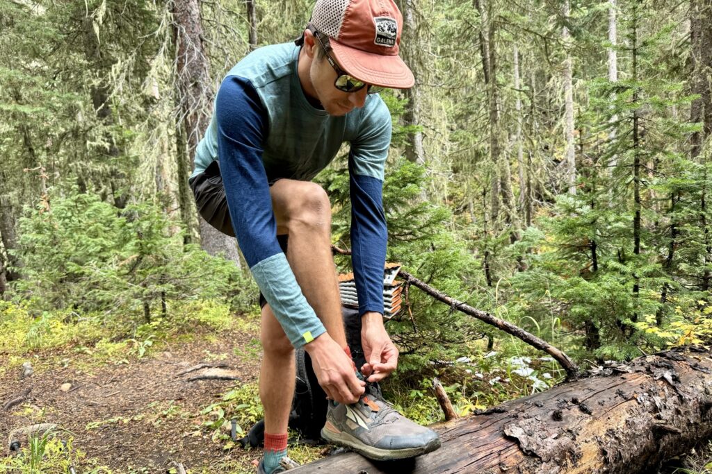 A hiker tying his shoe on a log in the woods while wearing the Ortovox Rock'n'Wool base layer.