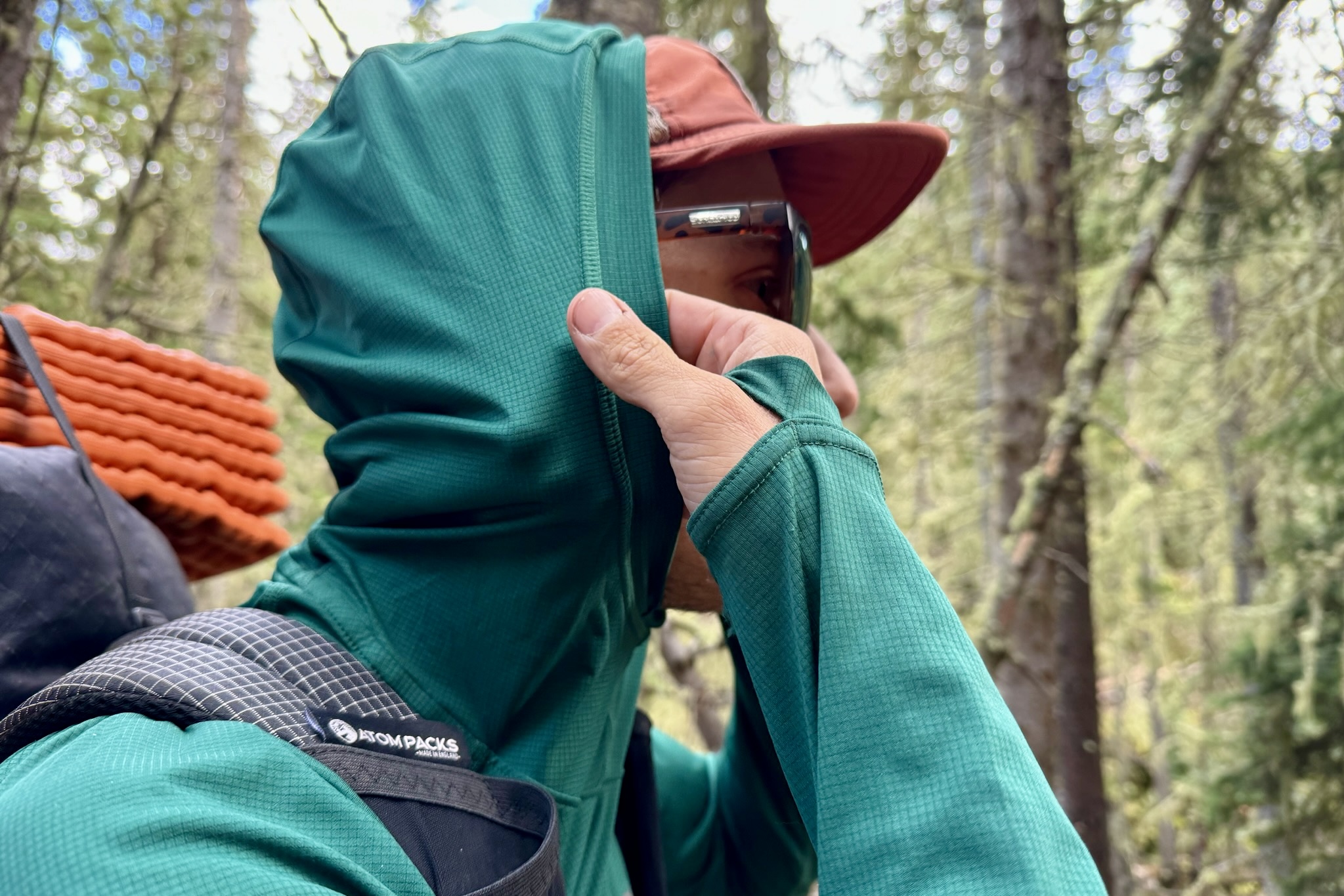 A hiker pulls up the hood on his Outdoor Research Echo Hoodie. Trees are in the background.