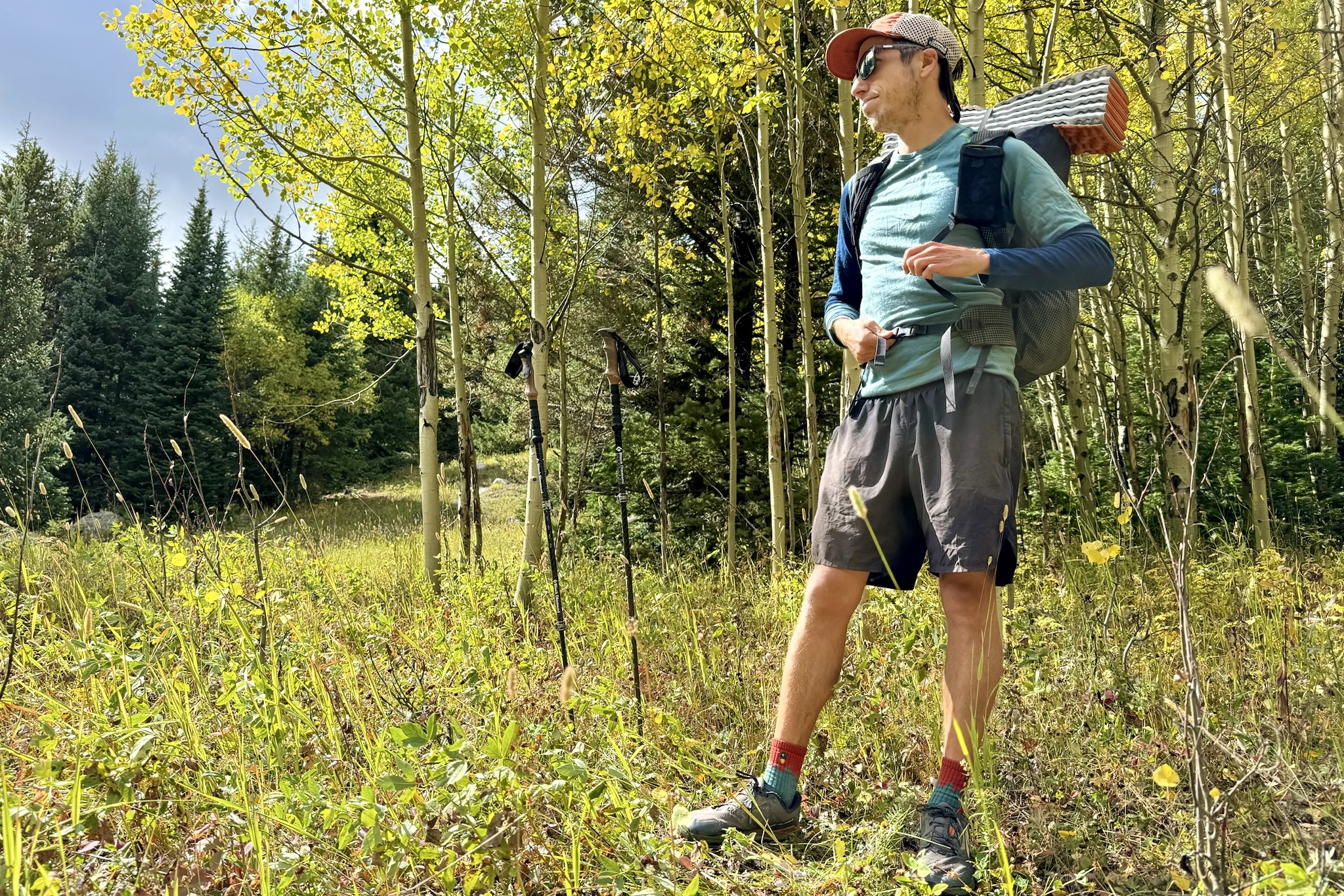 A hiker adjusting the buckles on his backpack straps while wearing the Rock'n'Wool base layer. Trees are in the background.