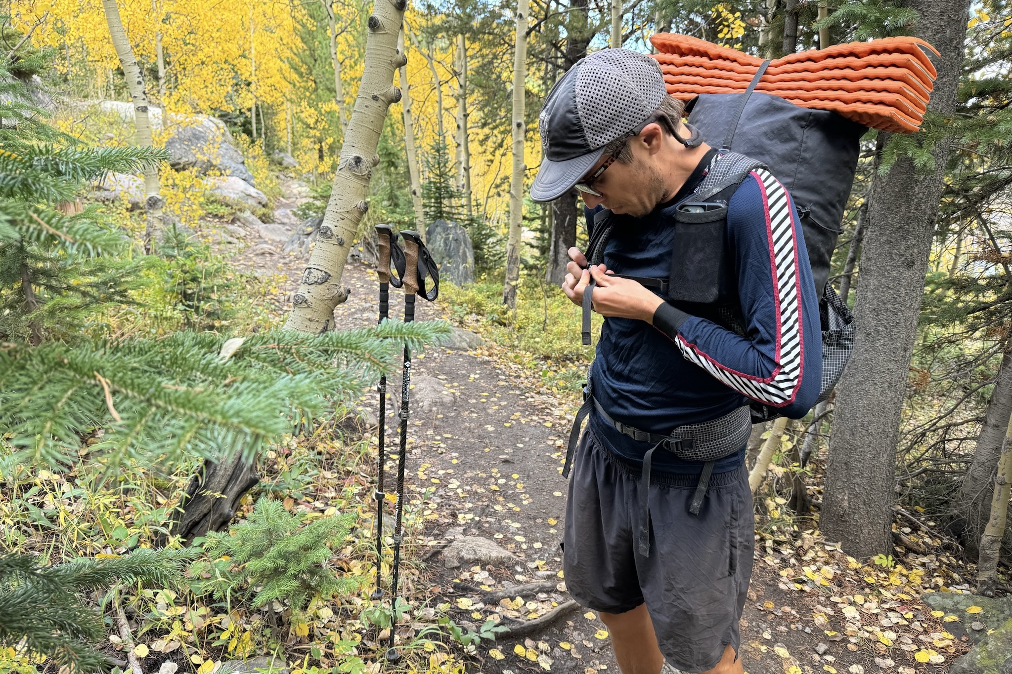 A hiker buckling the straps of his backpacking while wearing the Helly Hansen Lifa Stripe base layer. Trees and a trail are in the background.