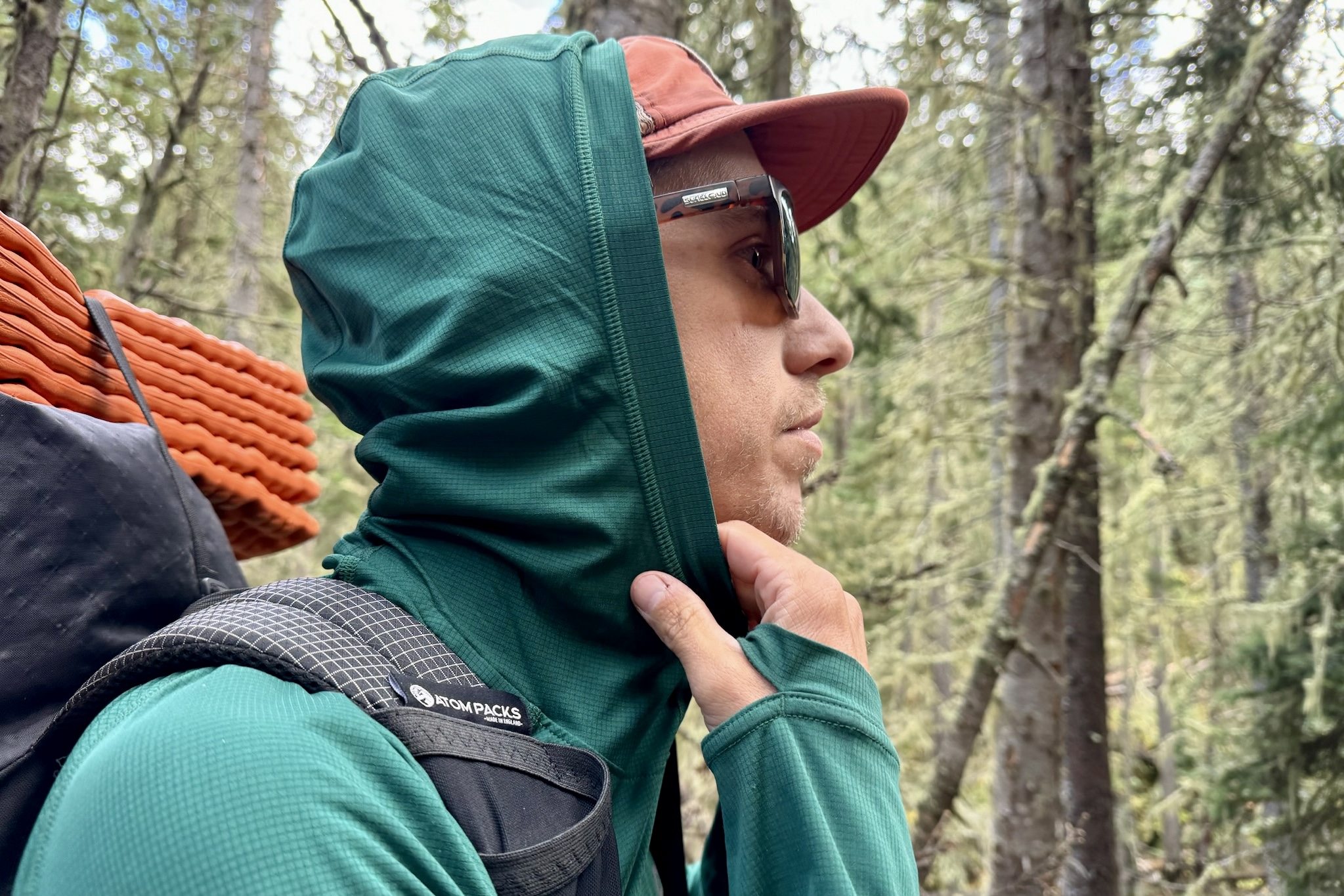 A hiker pulls up the hood on his Outdoor Research Echo Hoodie. Trees are in the background.