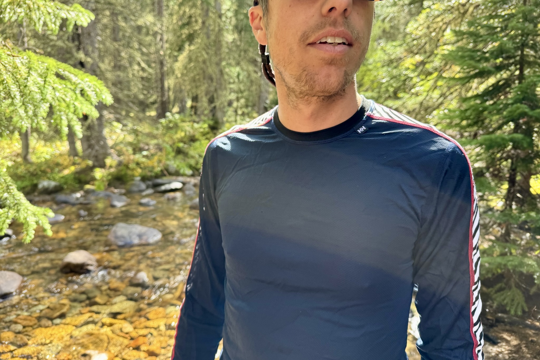 A closeup of a hiker's torso while wearing the Helly Hansen Lifa Stripe base layer. Trees and a creek are in the background.