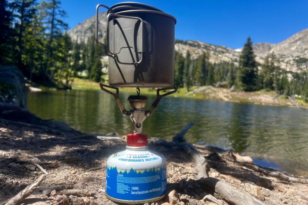 The PocketRocket 2 installed on a fuel canister and holding a pot with mountains and a lake in the background.