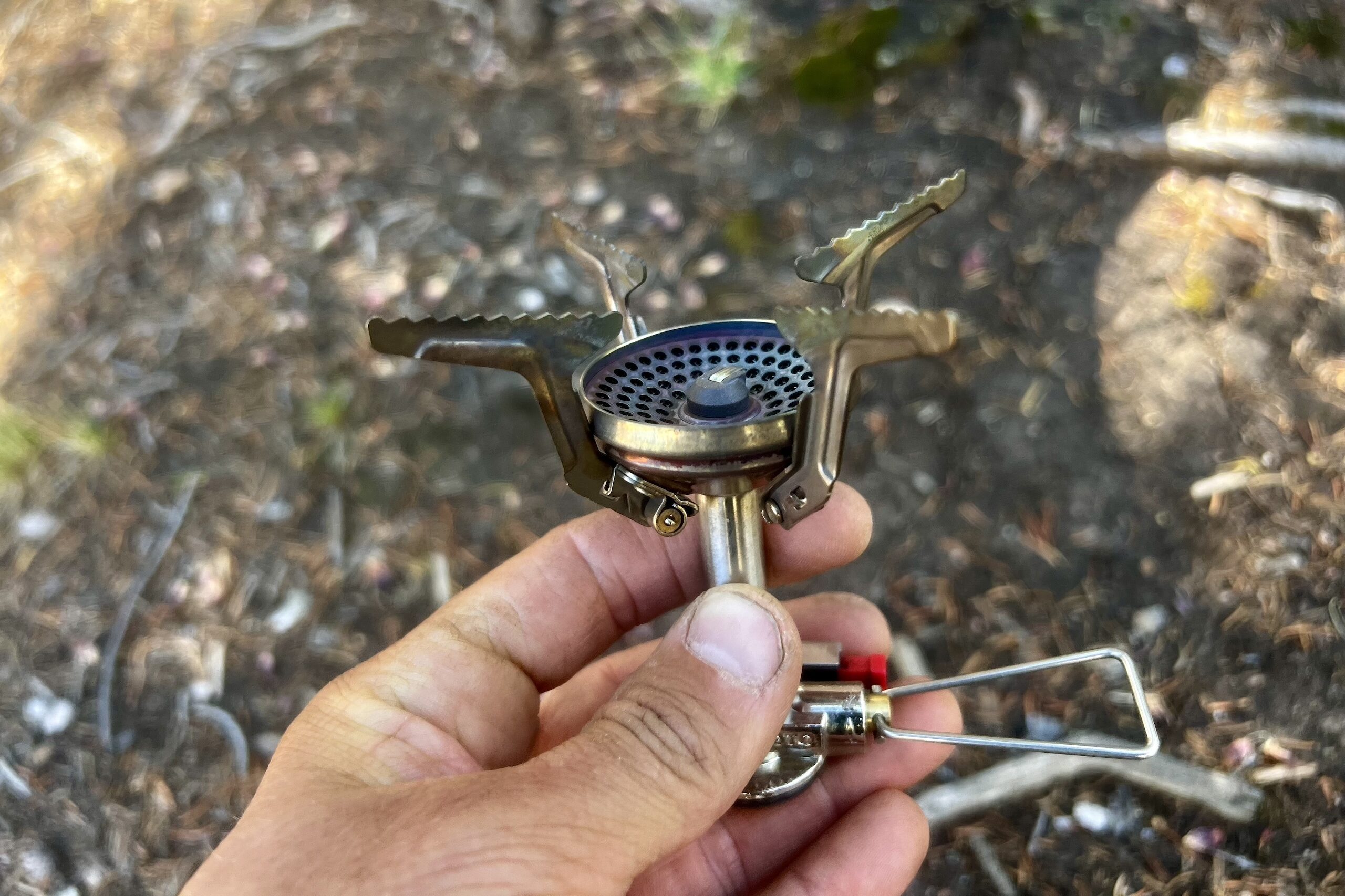 A closeup of a hand holding the SOTO Amicus Stove. The photo shows off the pot stand and burner, with the valve control in the shot as well.