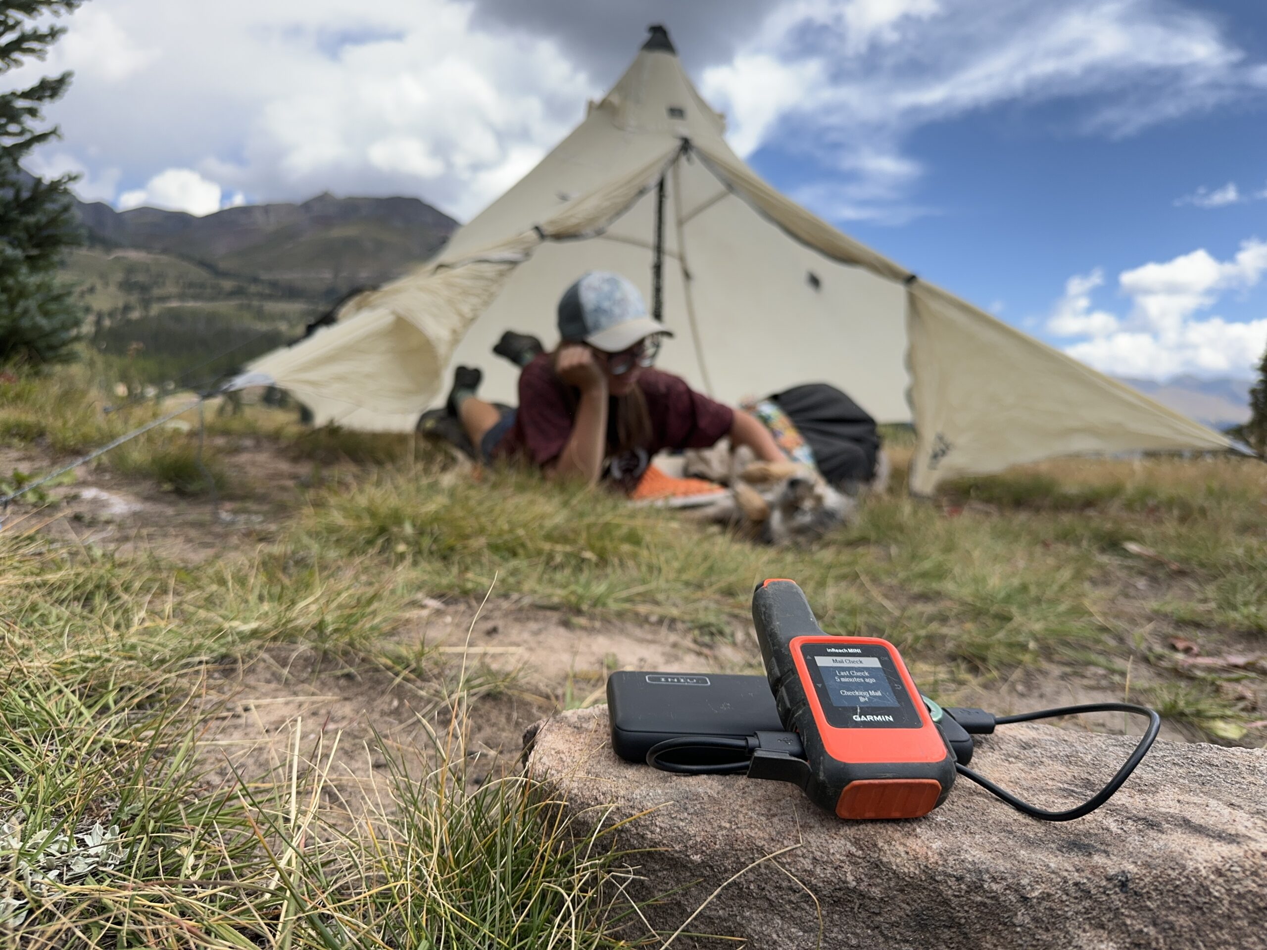 INIU Megapower 10000 charging a Garmin Inreach in the foreground with a person petting a dog inside a tent in the background.