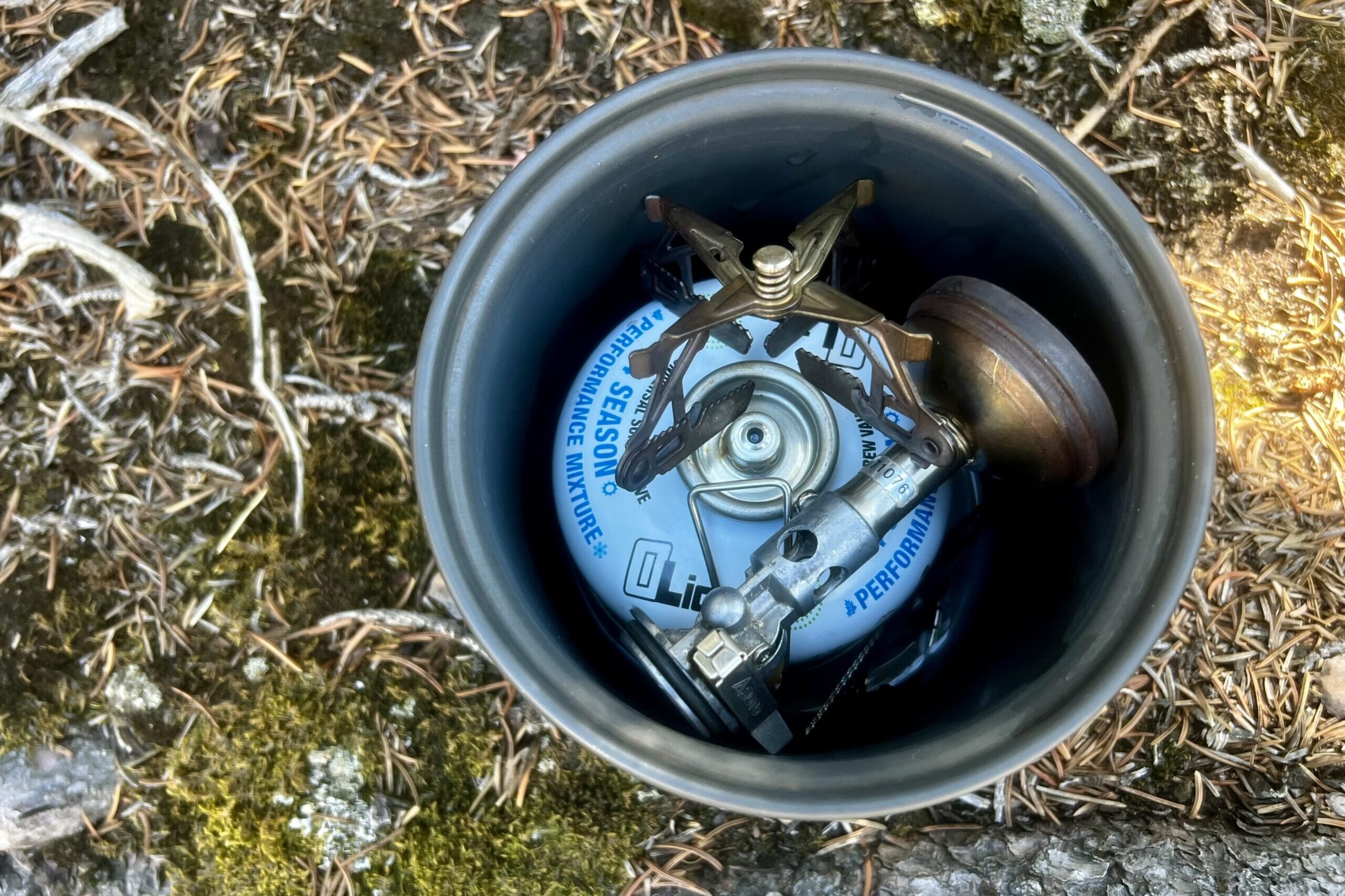 A top view of the SOTO WindMaster packed into a one liter pot with the 4Flex support and a small fuel canister. The pot sits on a mossy rock.