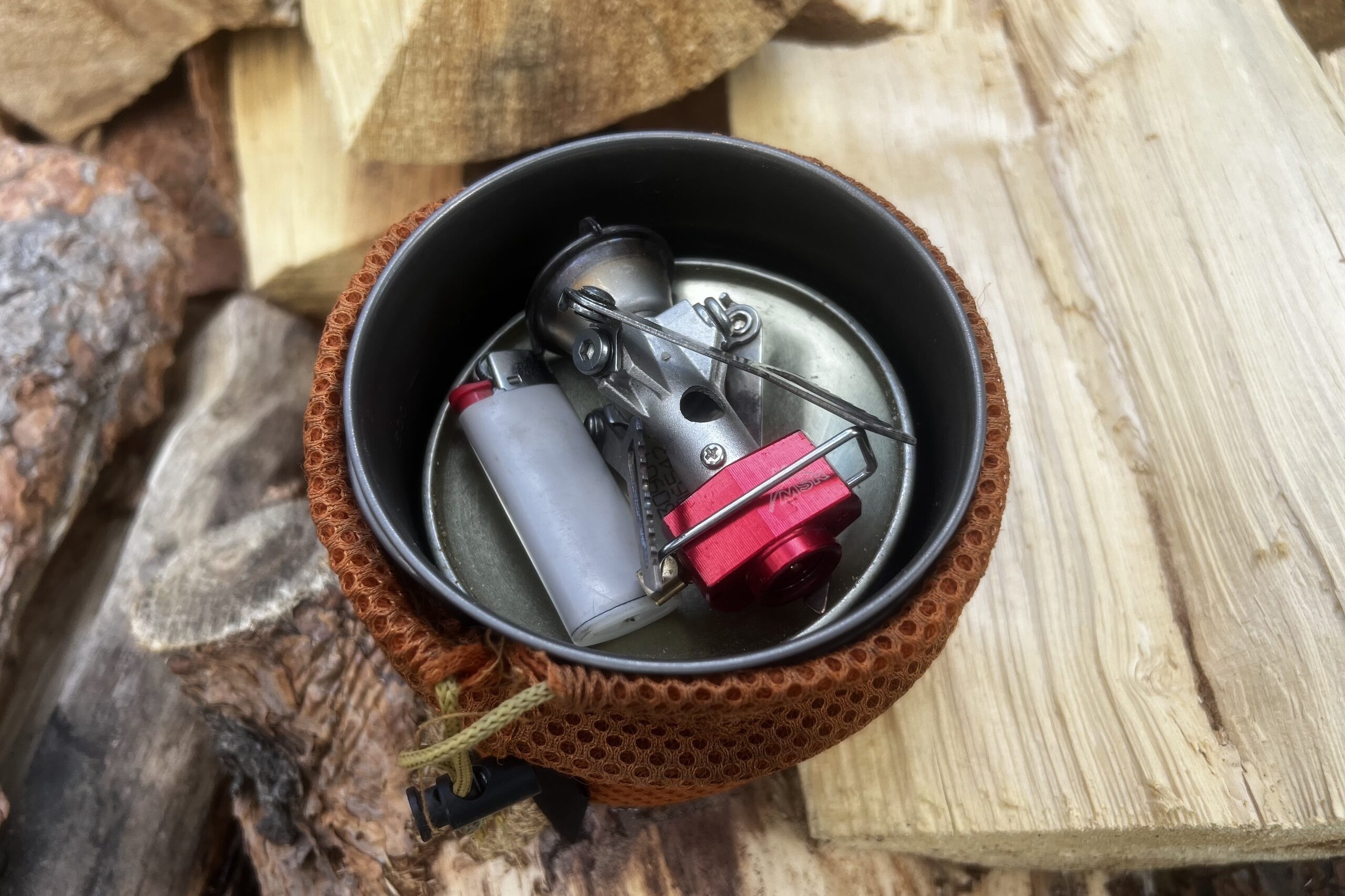 The MSR PocketRocket 2 packed in a pot with lighter and fuel canister, sitting on a pile of firewood