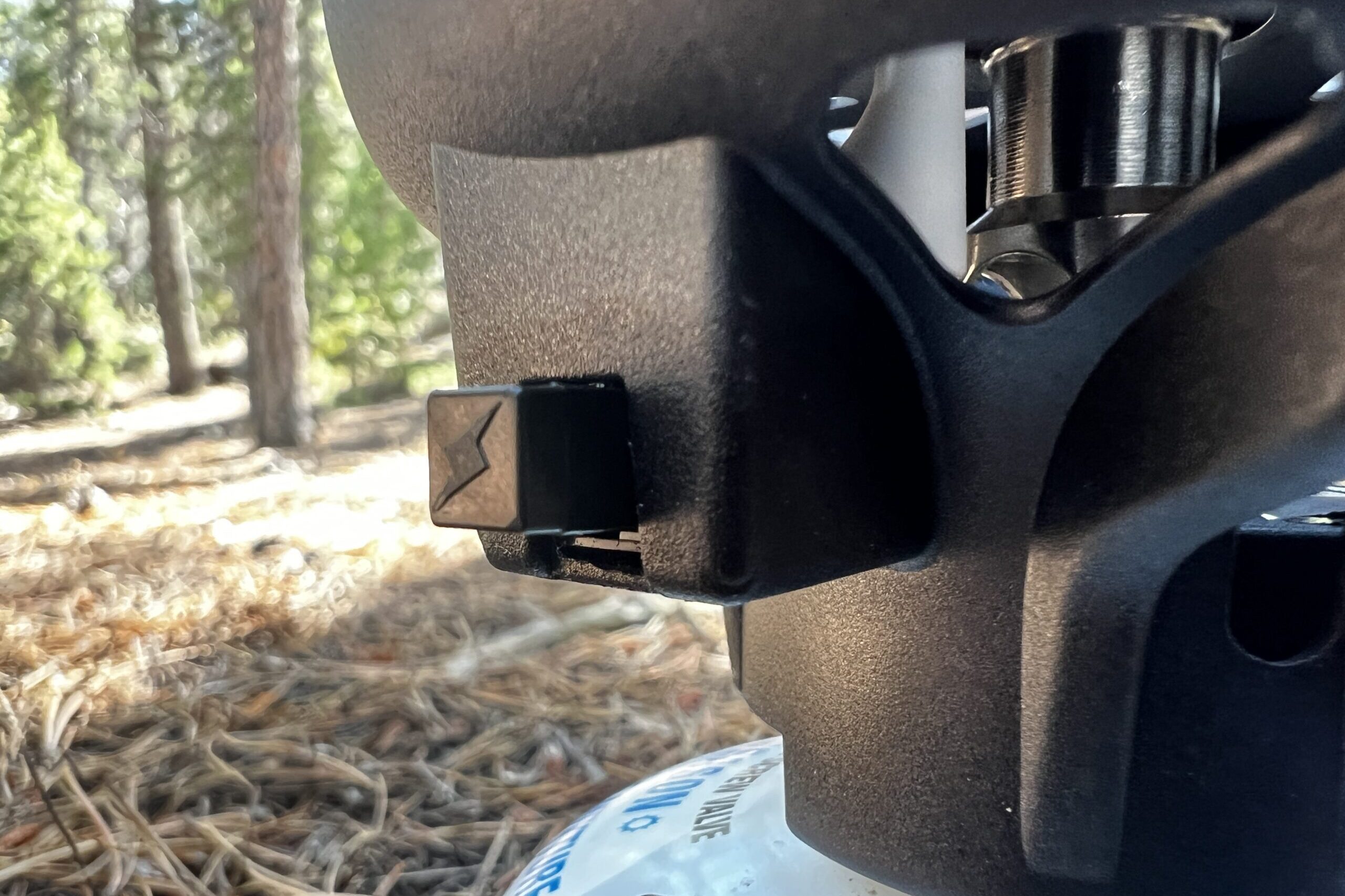 A very up close shot of the igniter switch on the JetBoil Flash. Trees and pine needles in the background.