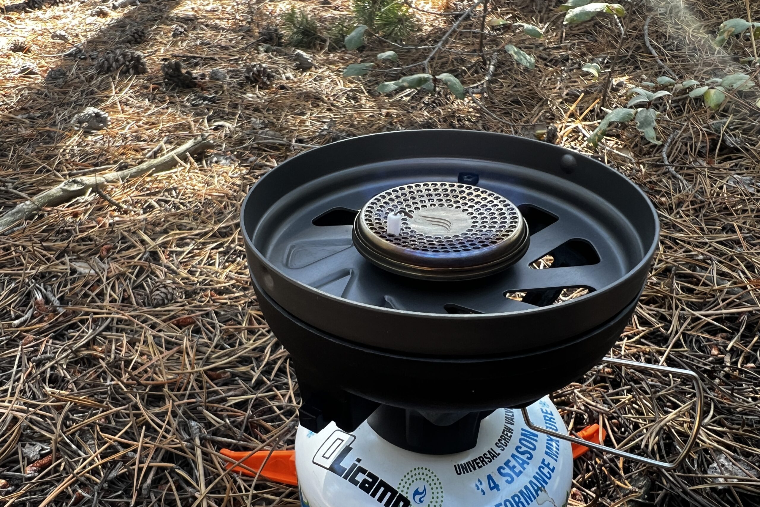 A close up, side shot of the burner of the JetBoil Flash. Also in the photo is the valve control, fuel support, and forest floor background.