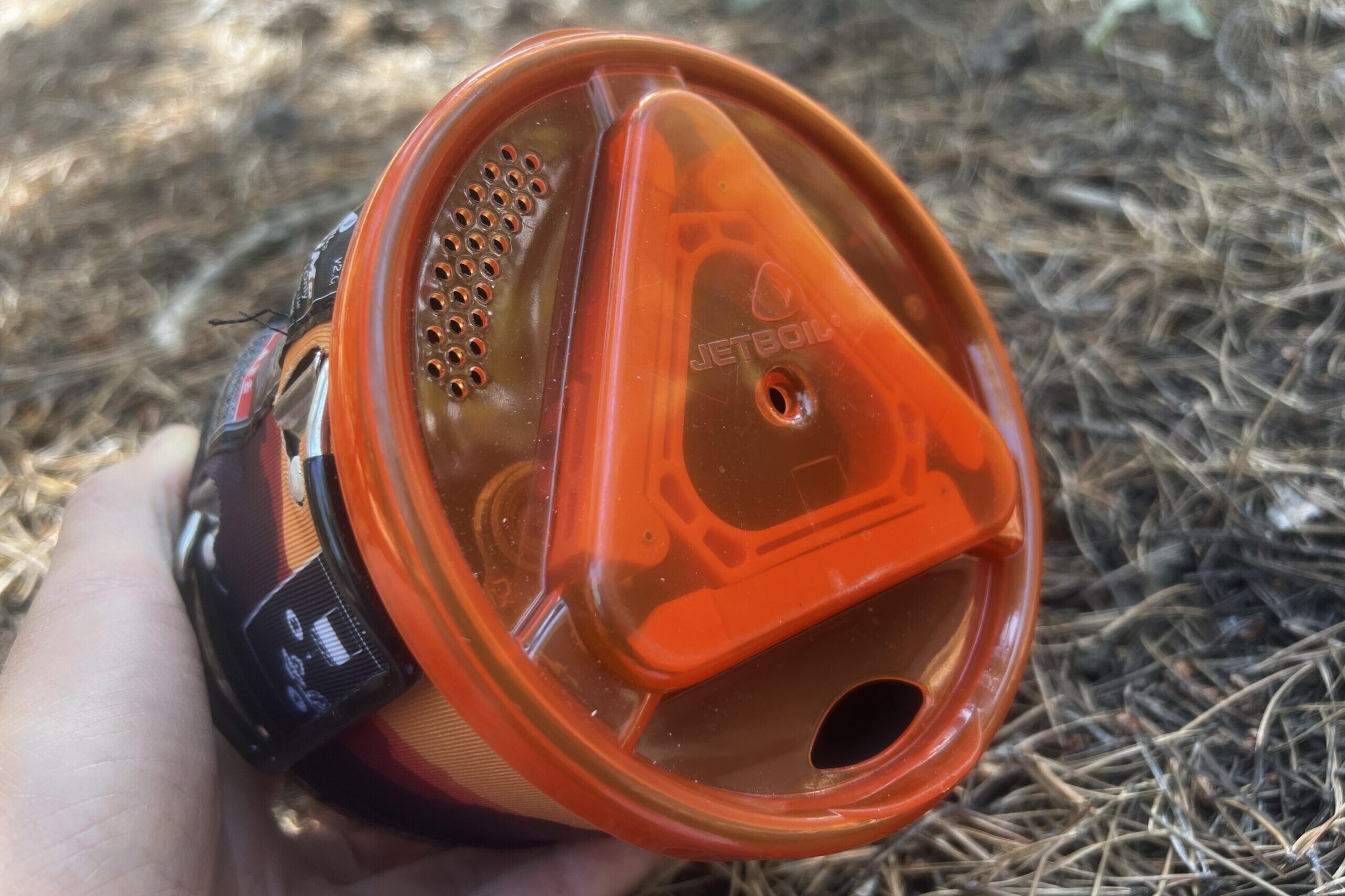 A close up, angled shot of the lid of the JetBoil MiniMo with pine needles in the background.