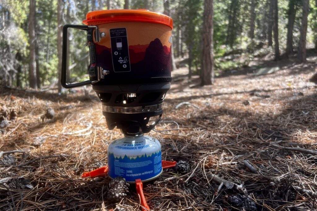 A profile shot of the MiniMo installed with burner, pot, fuel canister, and base support. Trees are in the background.