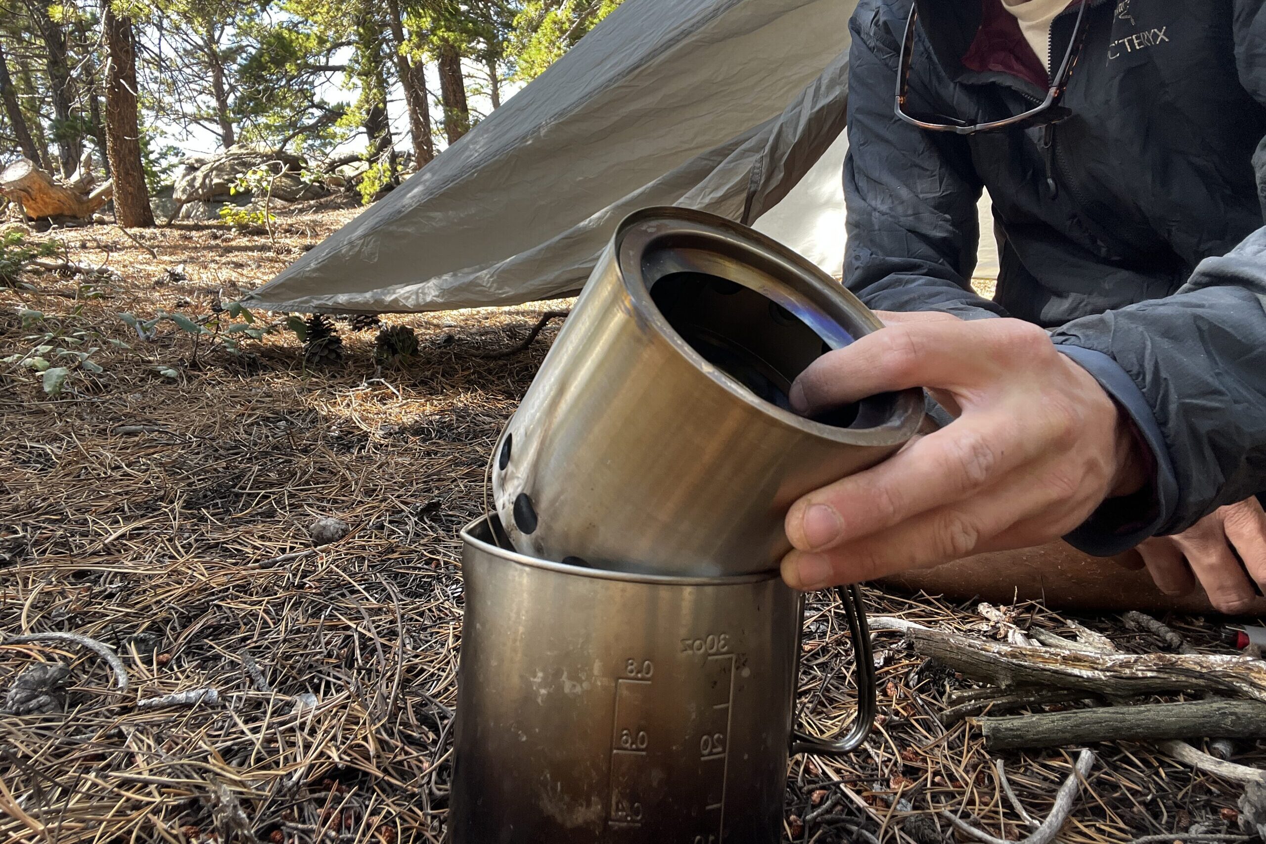 A hiker packed his Solo Stove Lite into a pot. A tent and trees are in the background.