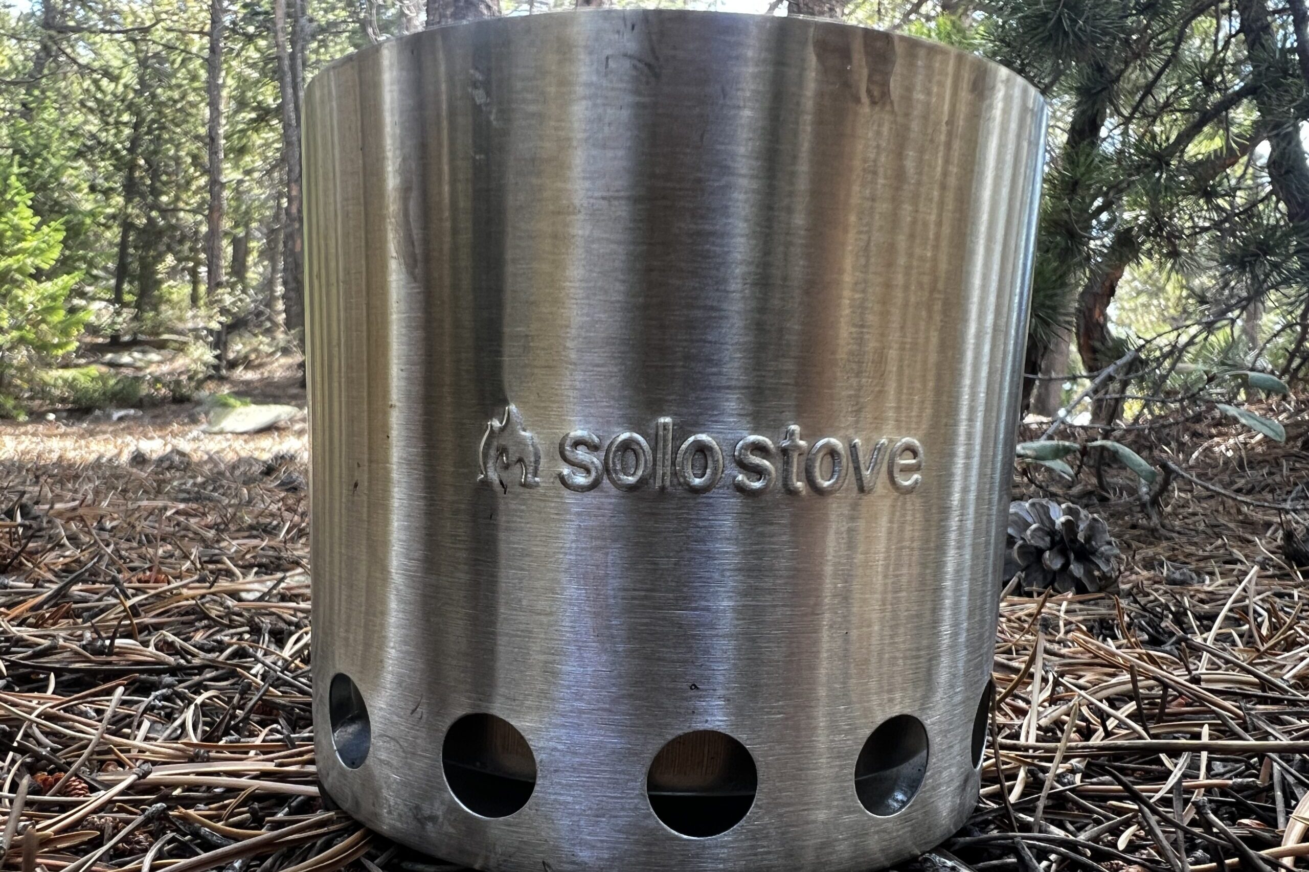 A close up of the Solo Stove Lite showing its air intake holes. Trees in the background.