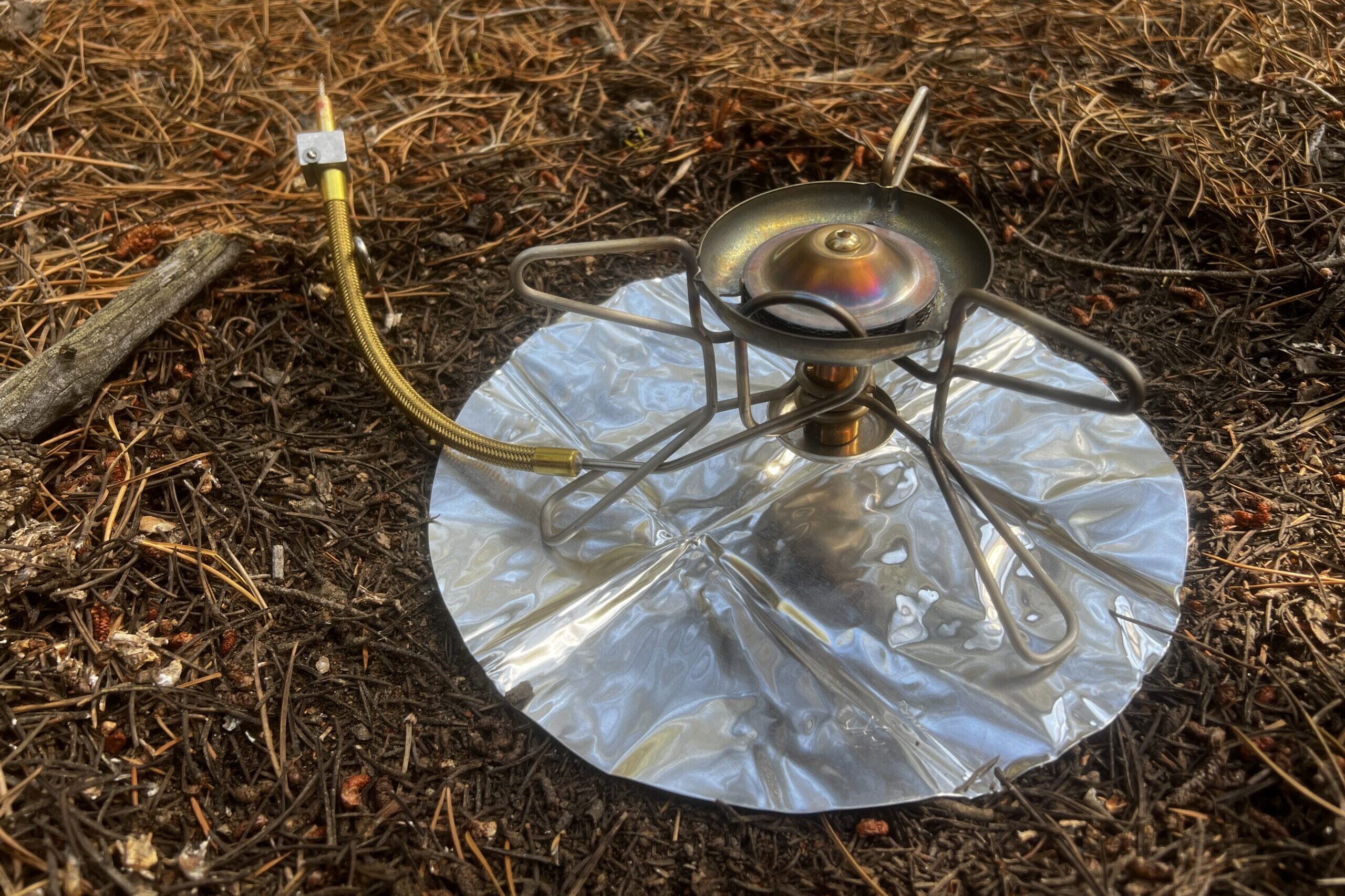 The Whisperlite sitting on its heat reflector with no fuel bottle attached. It sits on pine needles.