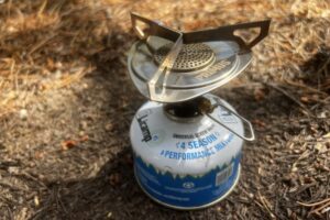 A close up of the whole Primus Essential Trail stove on a fuel canister with pine needs in the background.