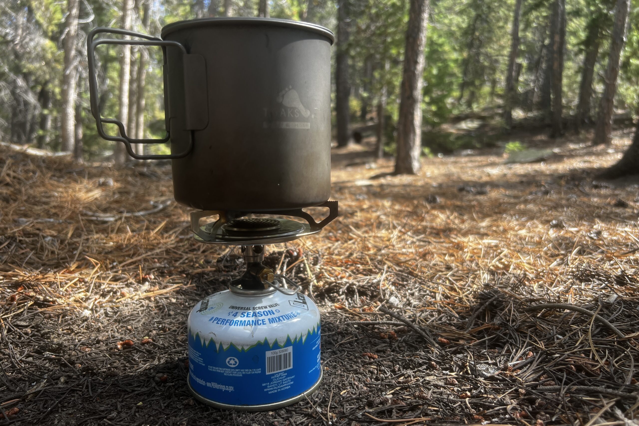 The Primus Essential Trail screwed on a fuel canister and holding a small pot. Trees are in the background.