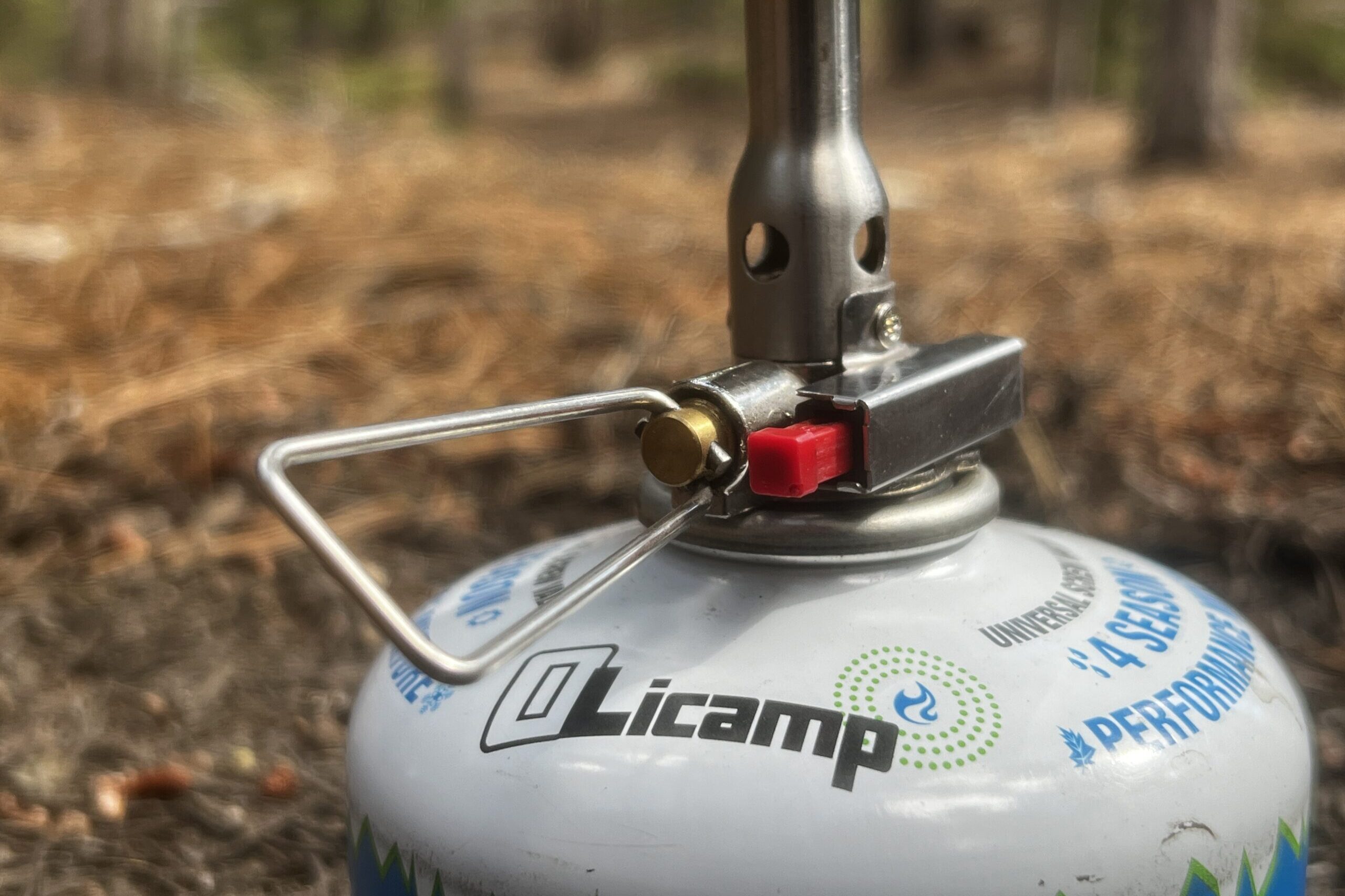 A close up of the valve control and igniter switch on the Amicus stove. The photo is on a blurred, treed background.