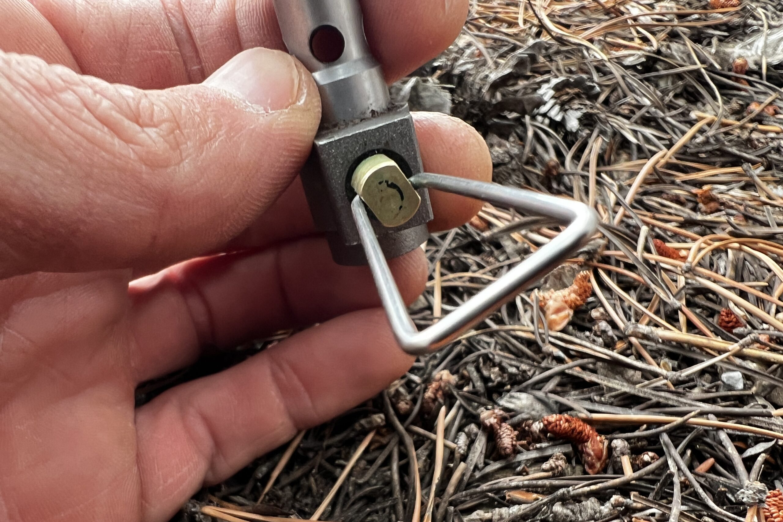 A hand holding the BRS 3000T showing a close up of the valve control. Pine needles in the background.