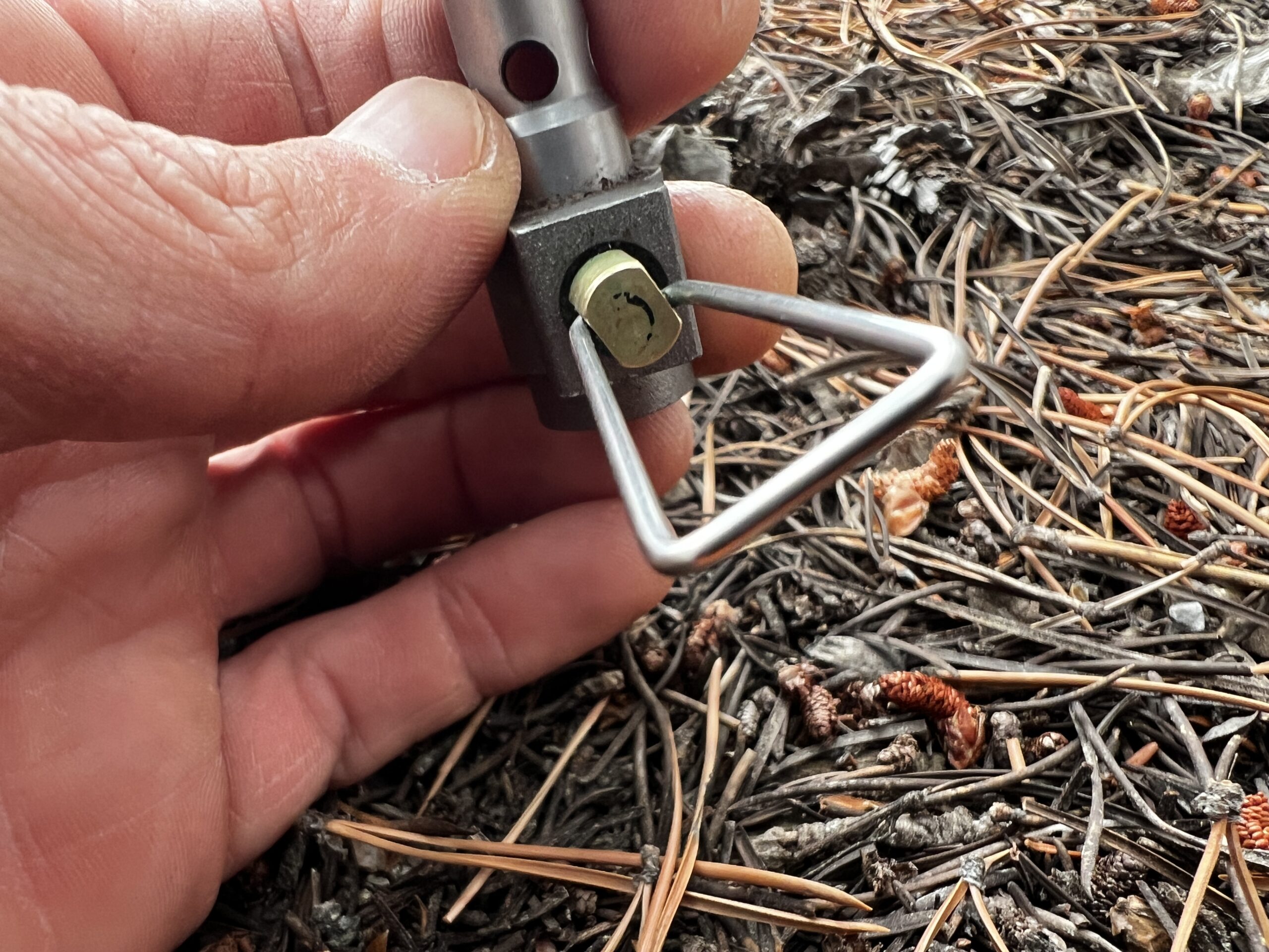 A hand holding the BRS 3000T showing a close up of the valve control. Pine needles in the background.