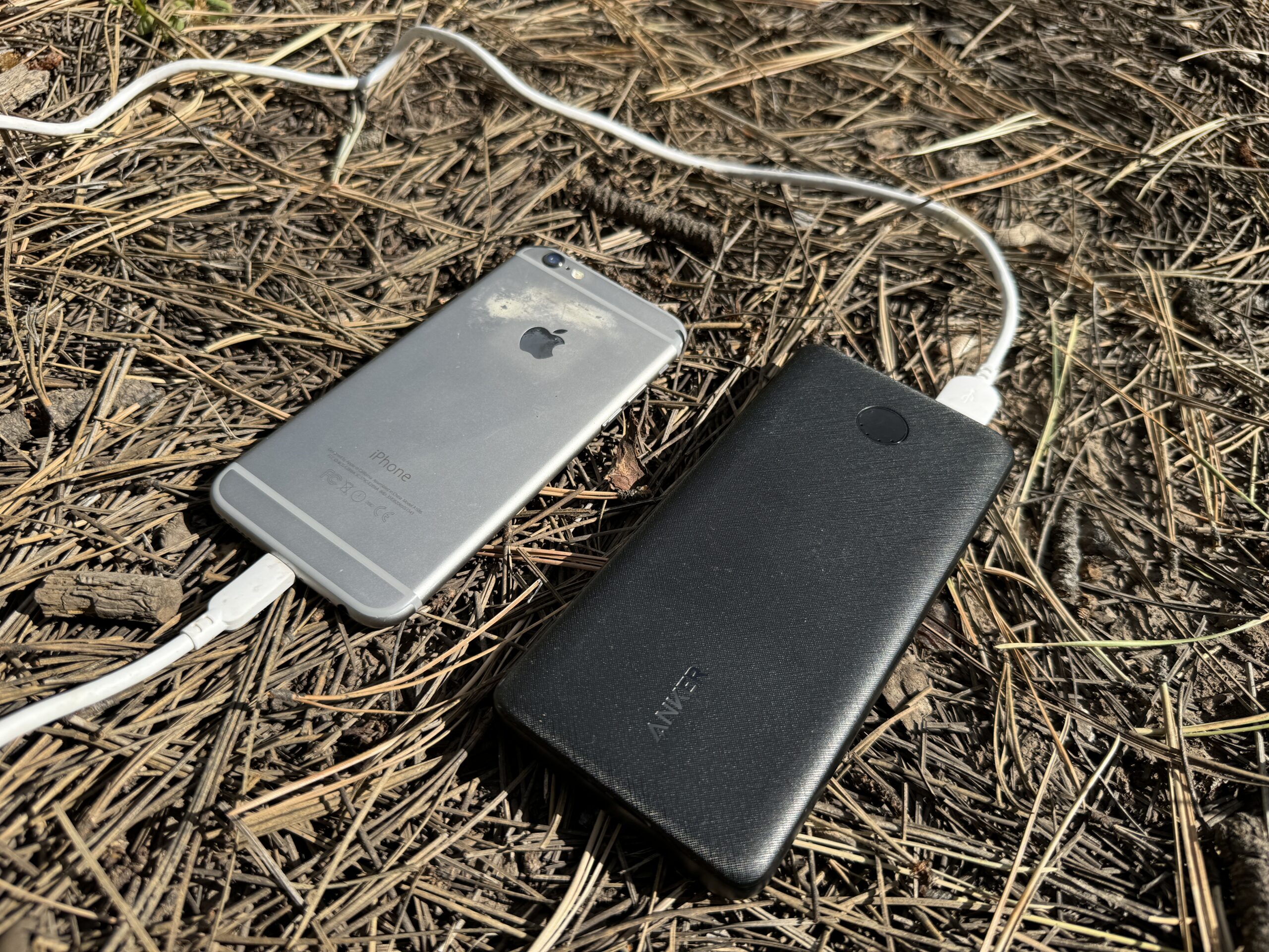 Close up of the Anker power bank charging a phone while sitting on some pine needles.