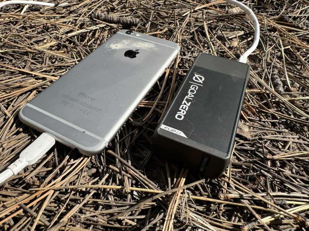 Close up of the Goal Zero power bank charging a phone while sitting on some pine needles.