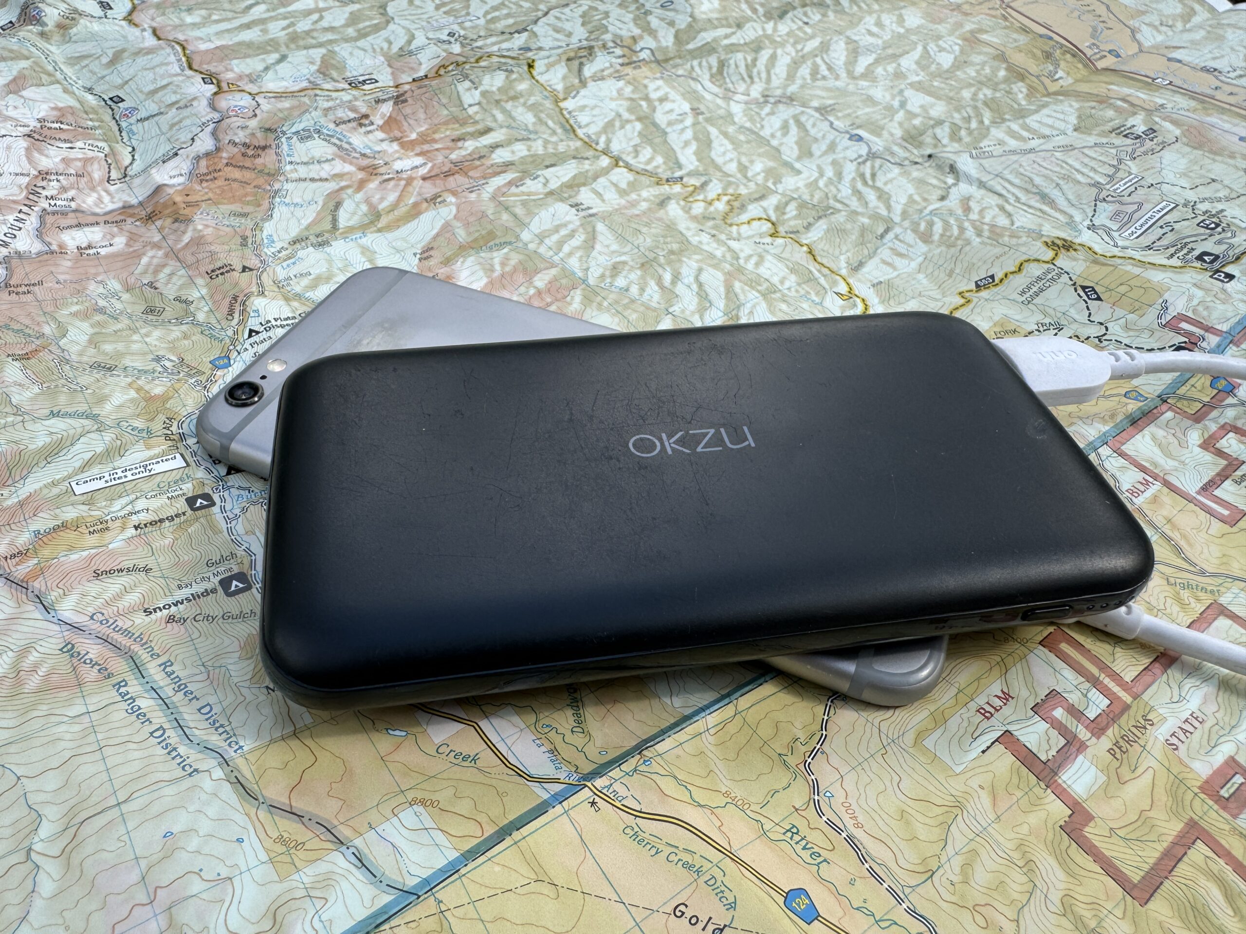 The OKZU power bank and a phone sit on a map.