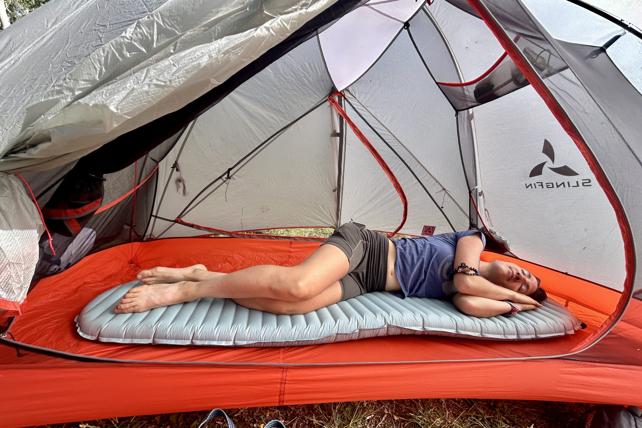 A woman rests comfortably on a grey sleeping pad in a red tent.