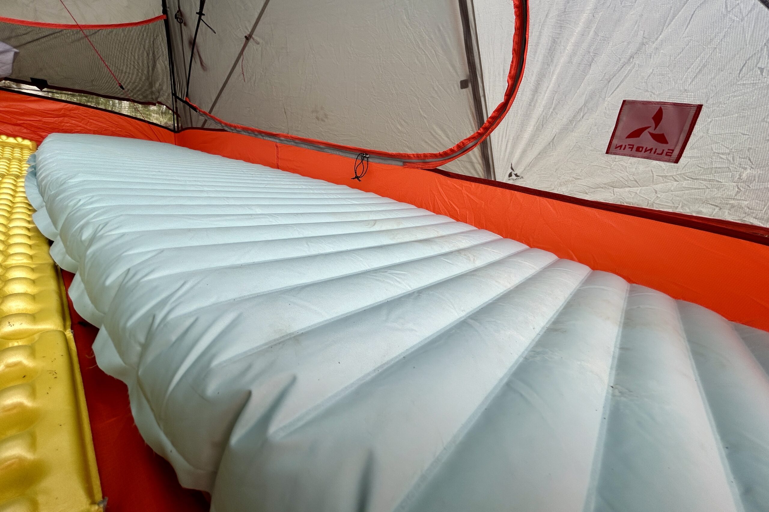 Close up of the horizontal baffles of an inflated sleeping pad in a red tent.