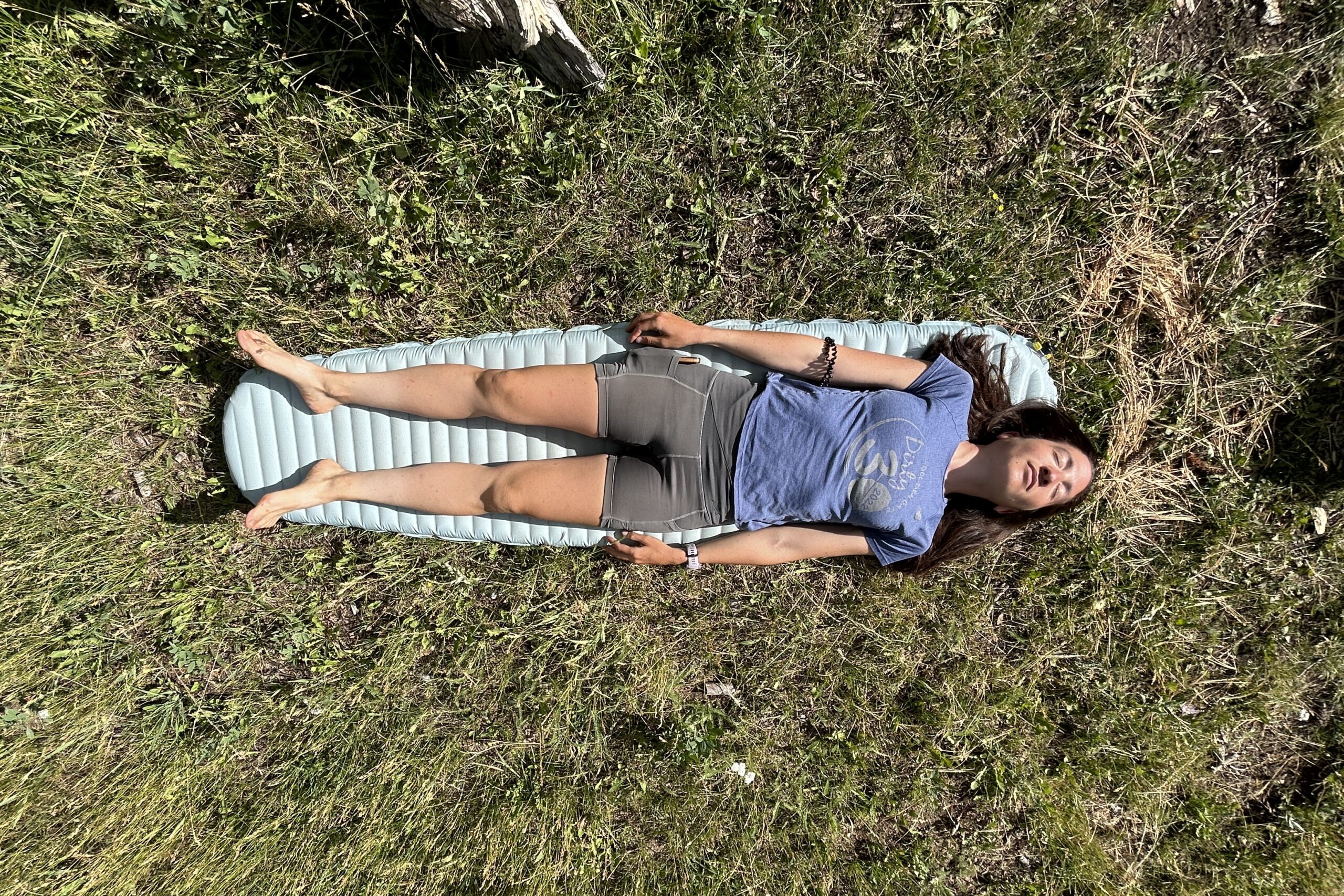 A woman is lying on an inflatable mattress in the grass on a sunny day.