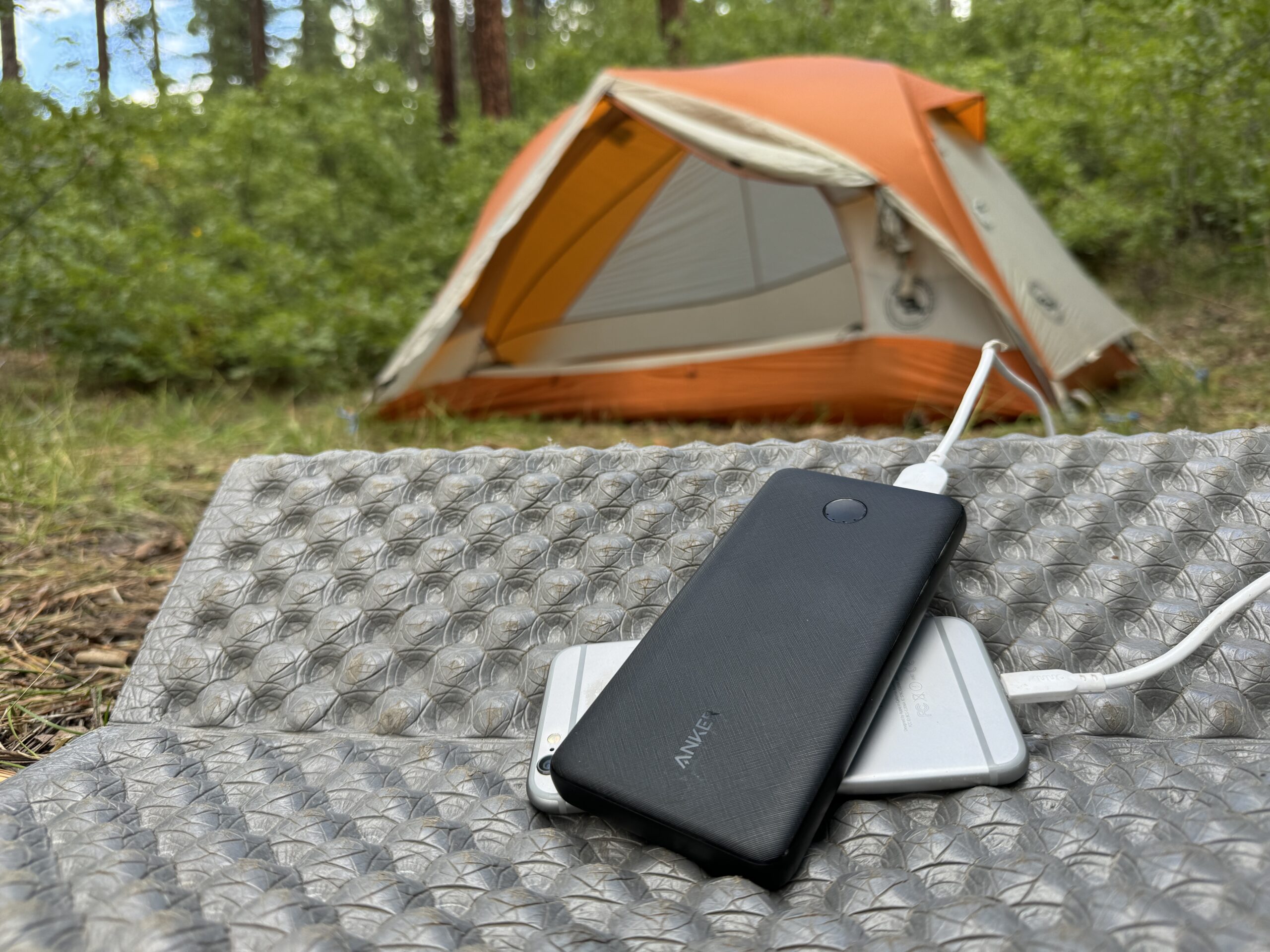 The Anker and a phone sit in front of a tent in the woods.