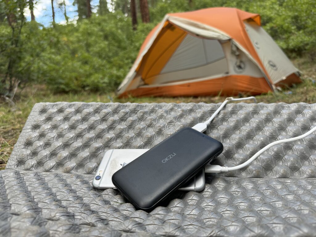 The OKZU and a phone sit in front of a tent in the woods.