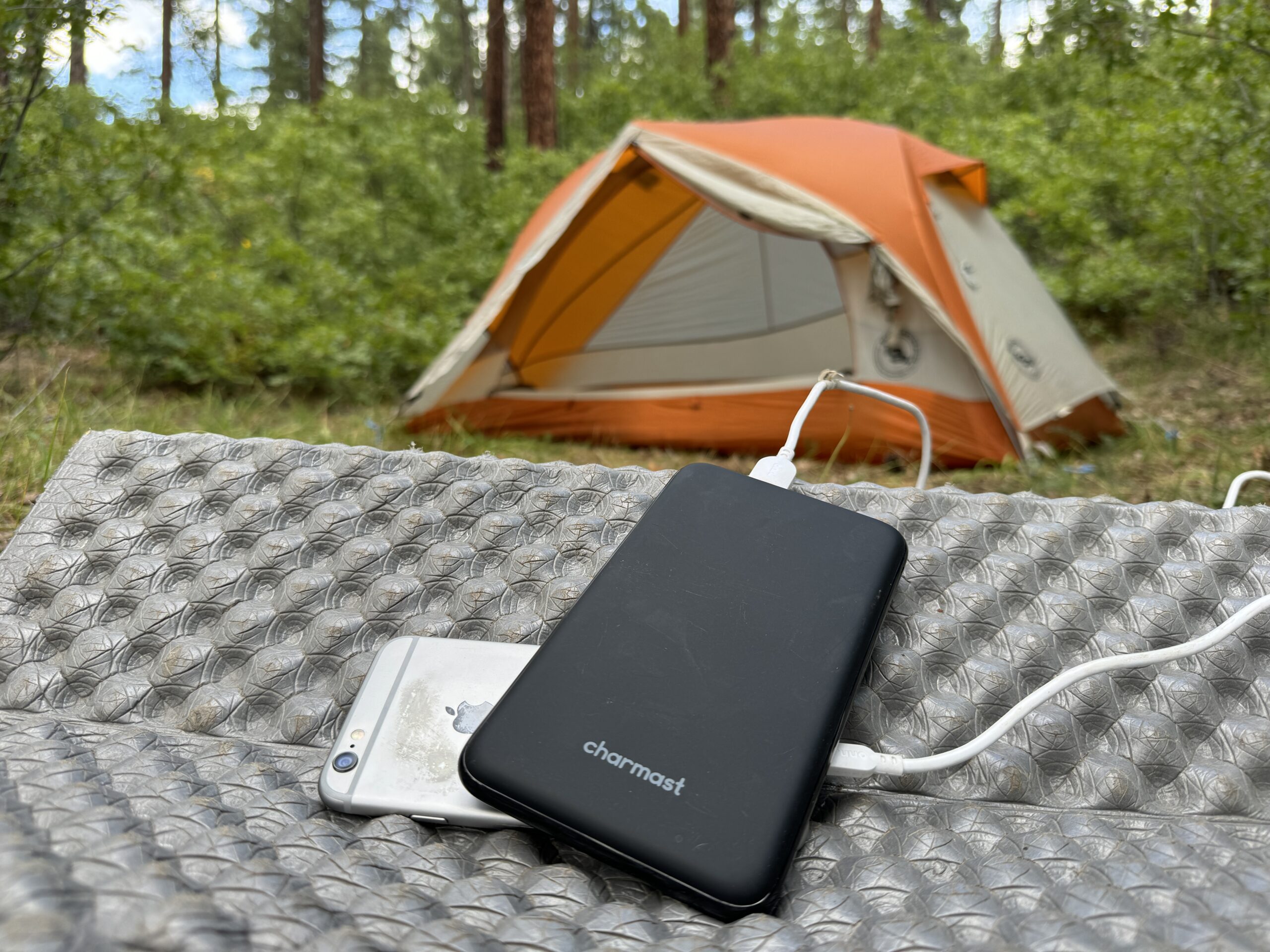 The Charmast and a phone sit in front of a tent in the woods.