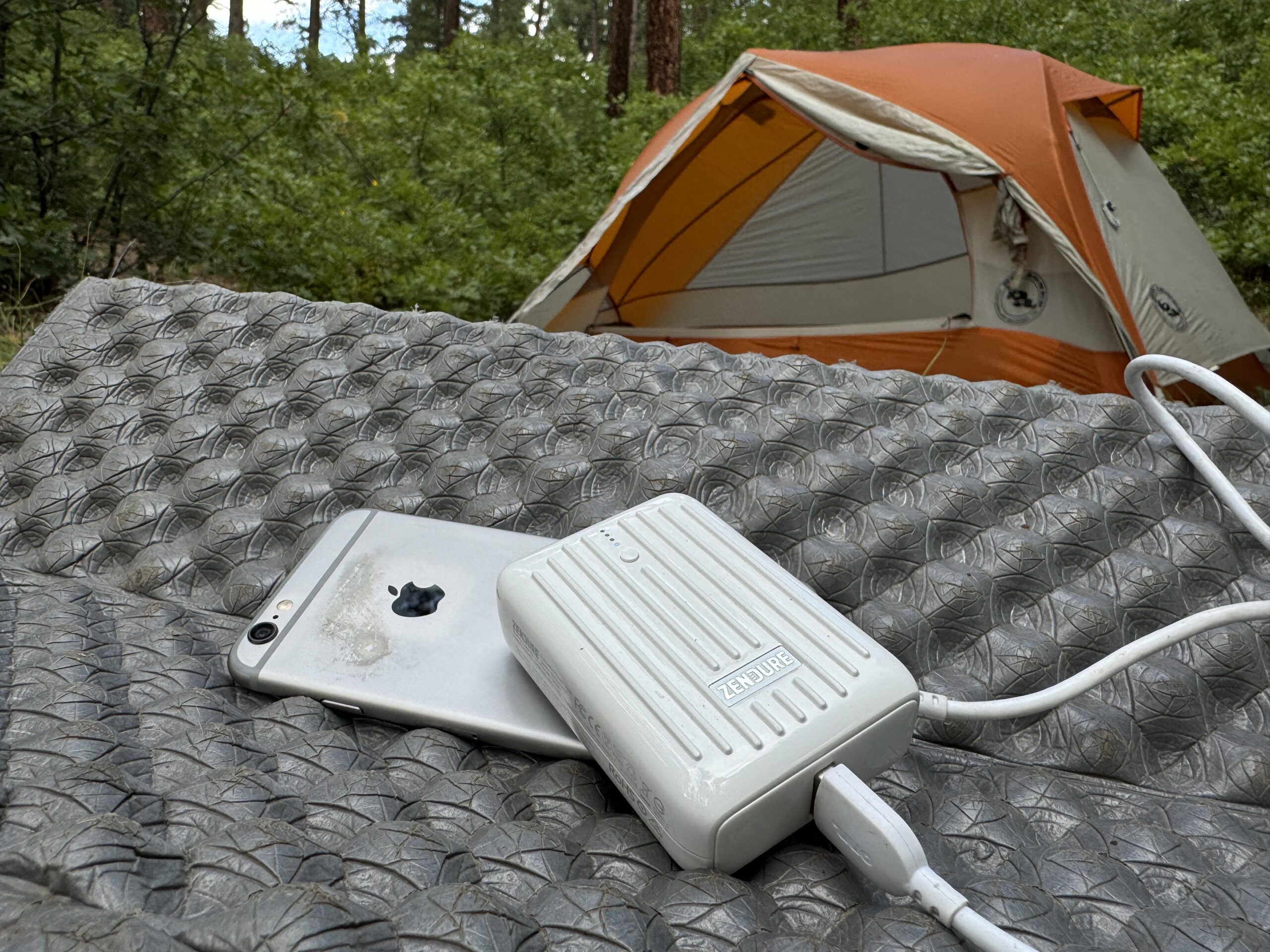 The Zendure and a phone sit in front of a tent in the woods.