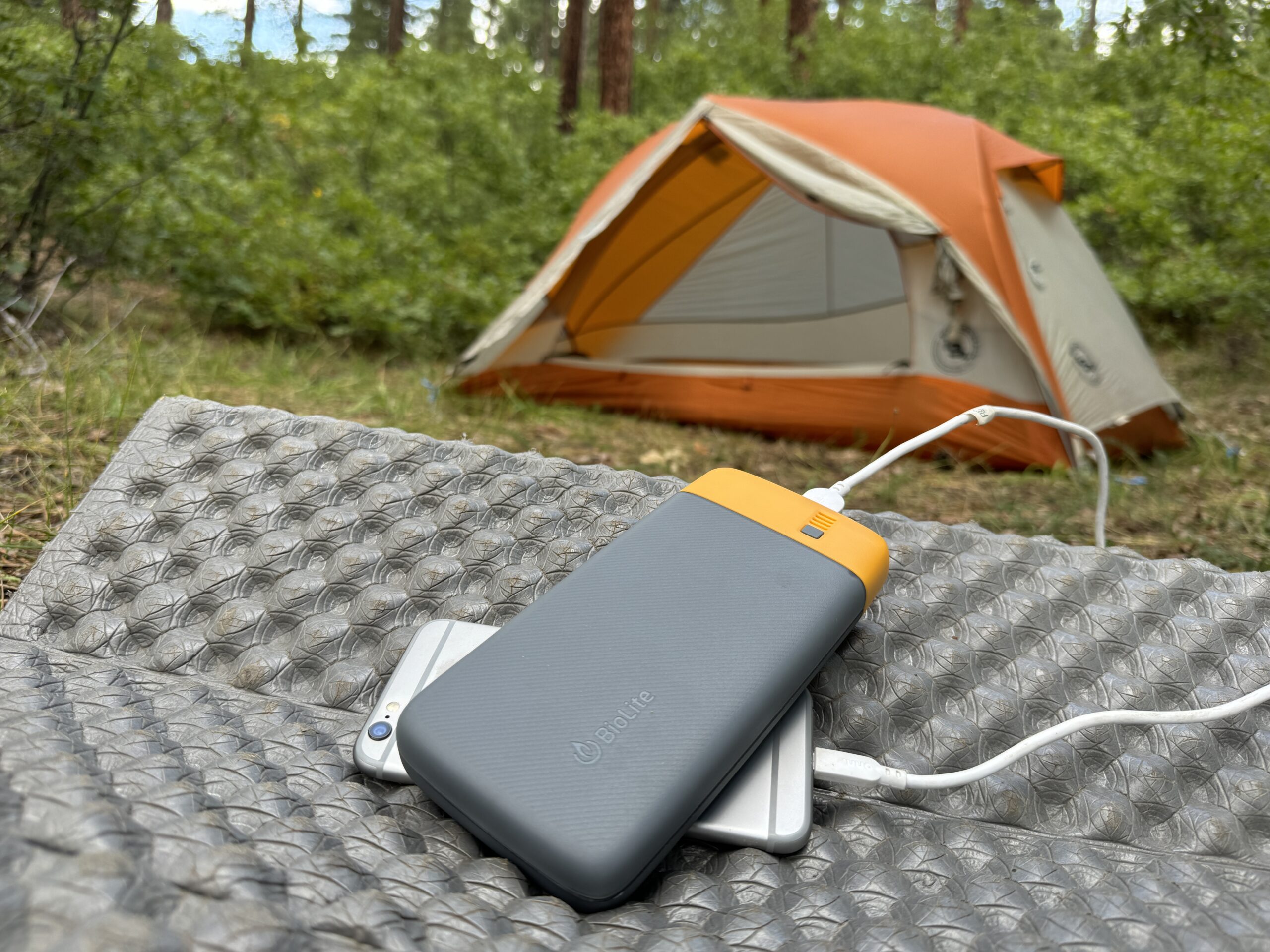 The BioLite and a phone sit in front of a tent in the woods.