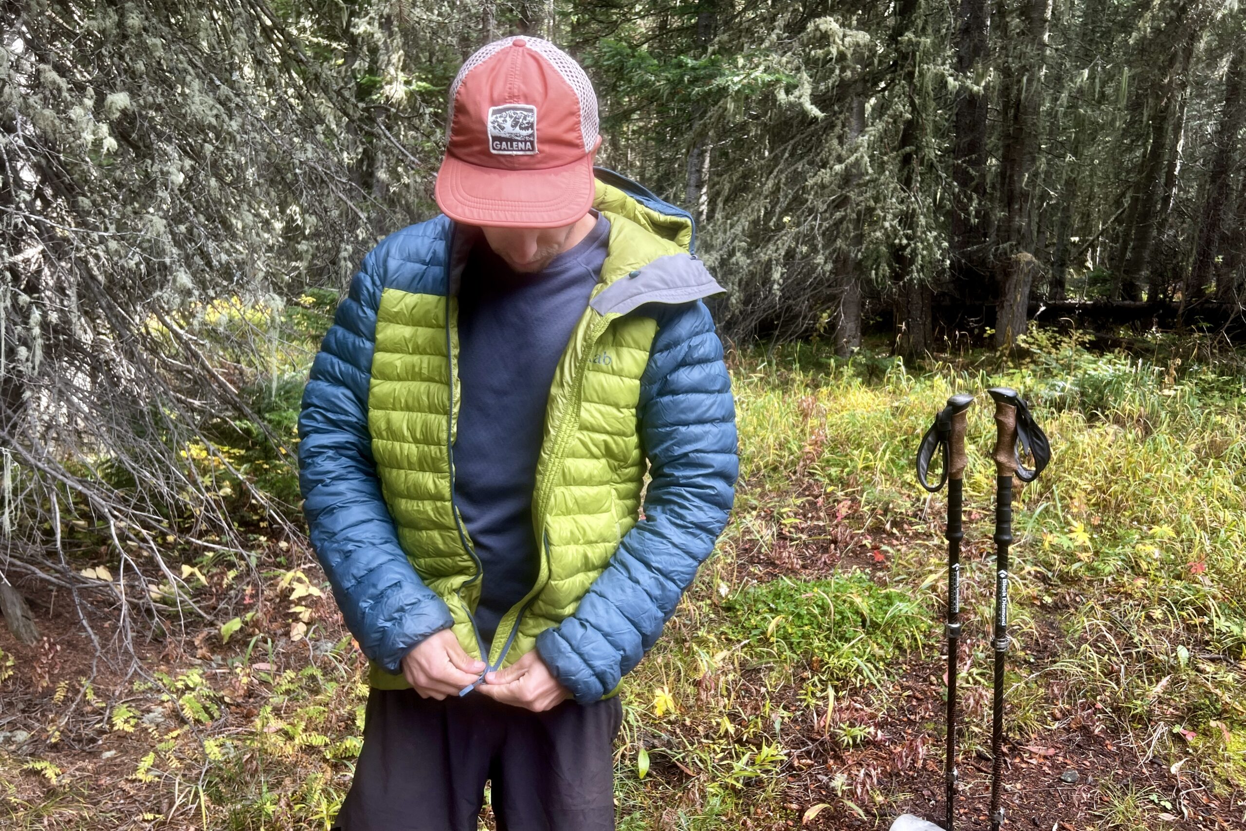 A hiker zips up a puffy jacker over the Patagonia Capilene Midweight Crew. Trees and trekking poles are in the background.