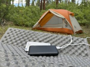 The Miady and a phone sit in front of a tent in the woods.