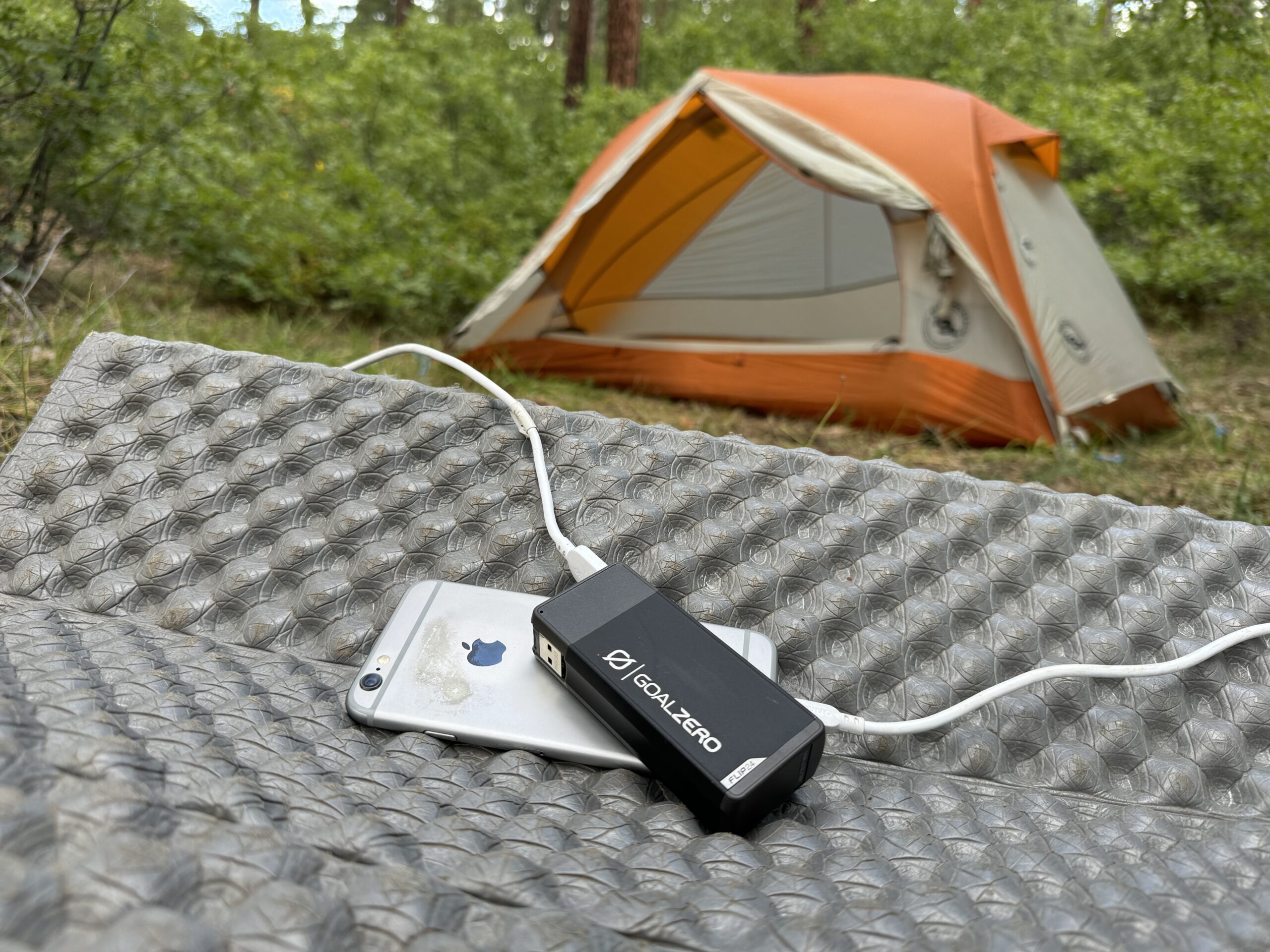 The Goal Zero and a phone sit in front of a tent in the woods.