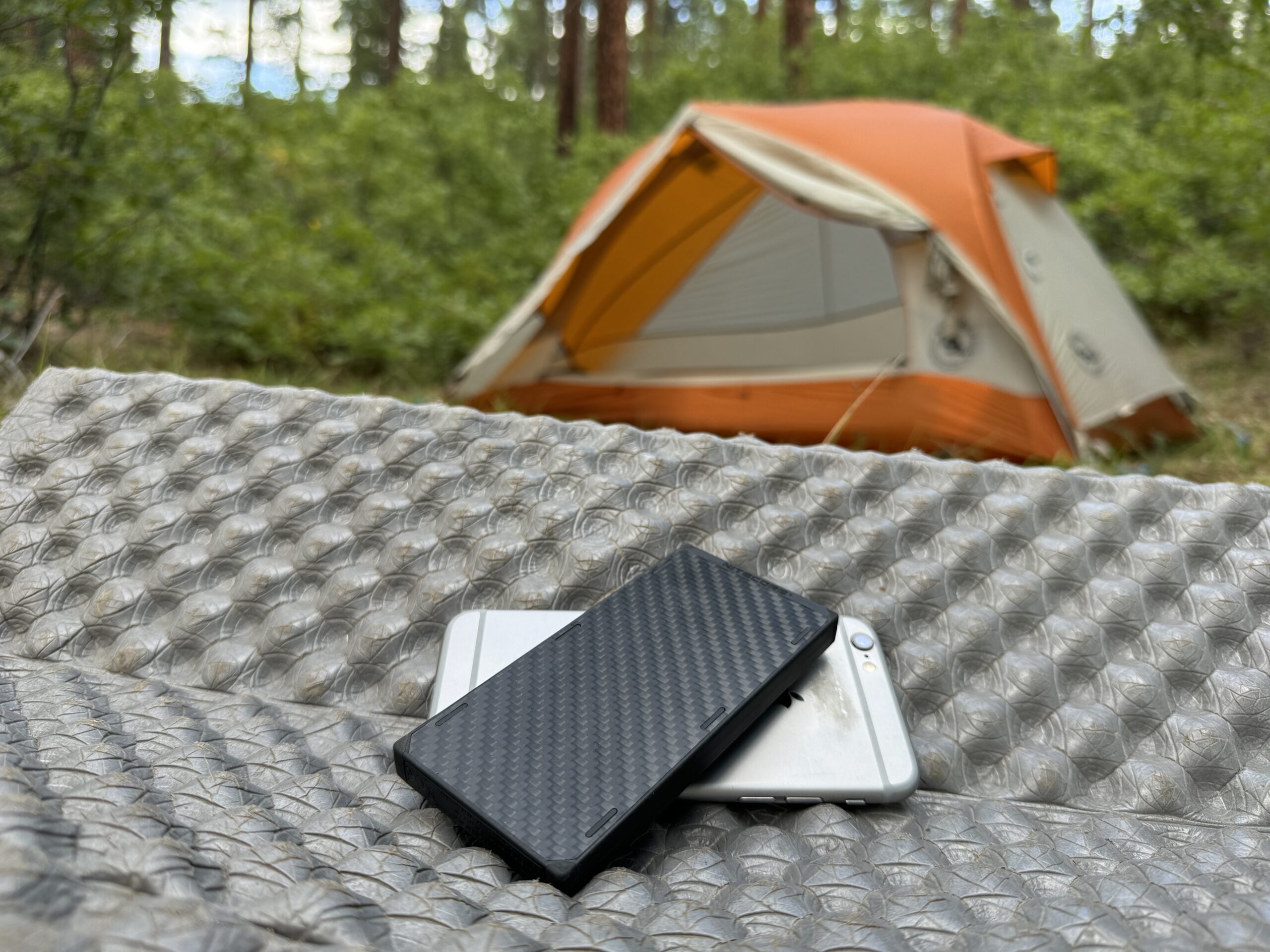 The Nitecore and a phone sit in front of a tent in the woods.