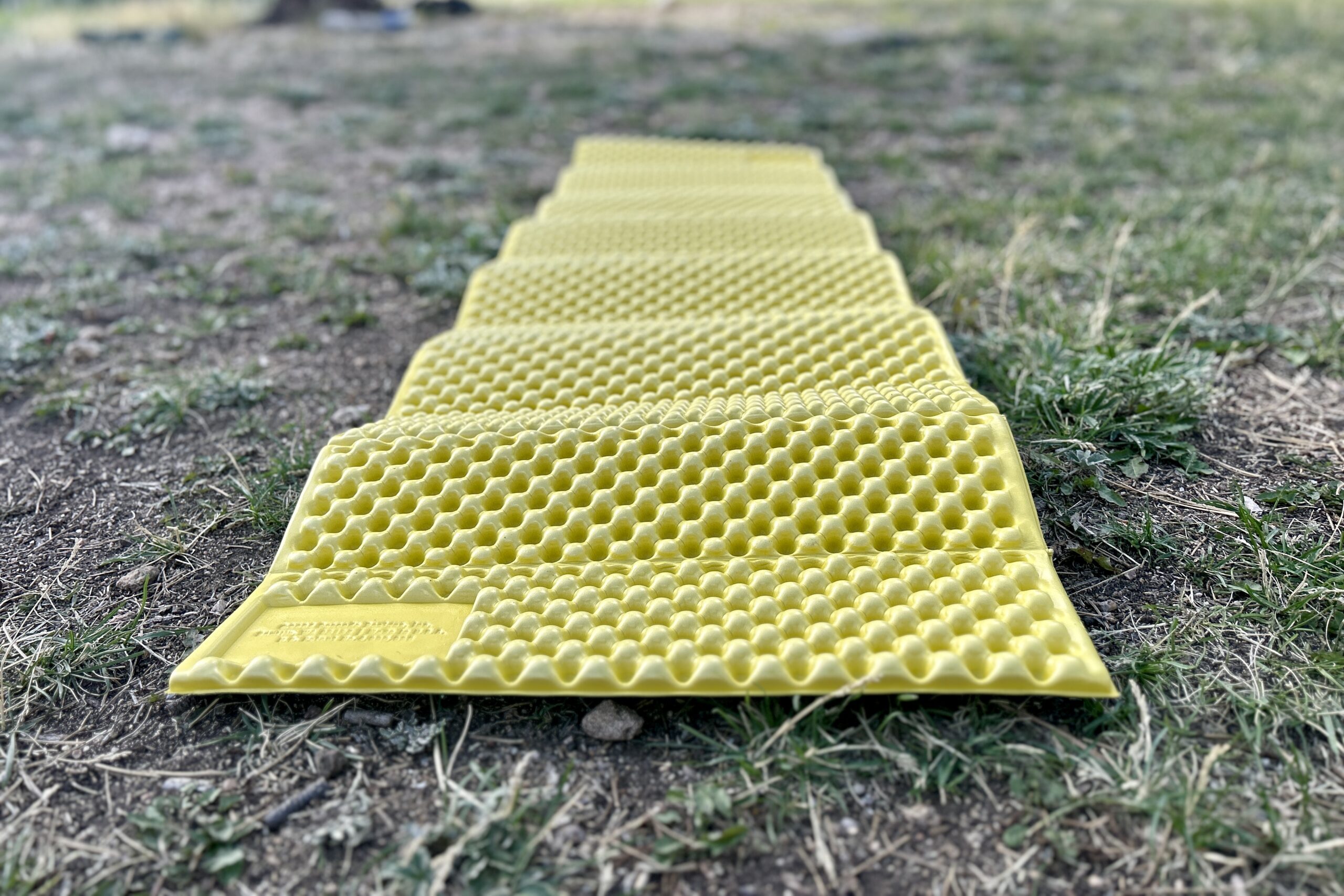 Close up of a yellow foam mat laying on the ground showing its bumpy texture.