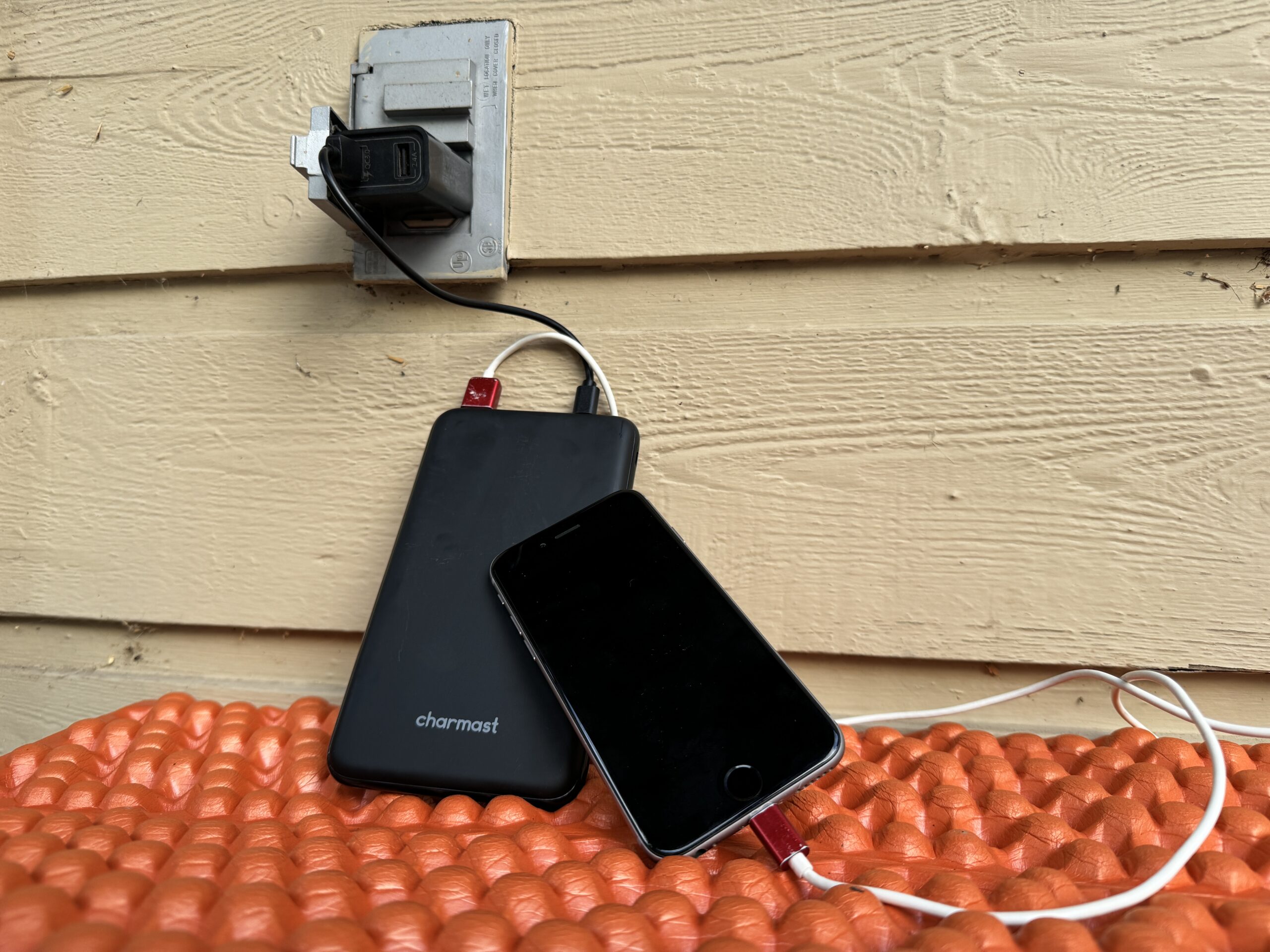 Close up of the Charmast charging from an outlet and a cell phone charging from the power bank simultaneously.