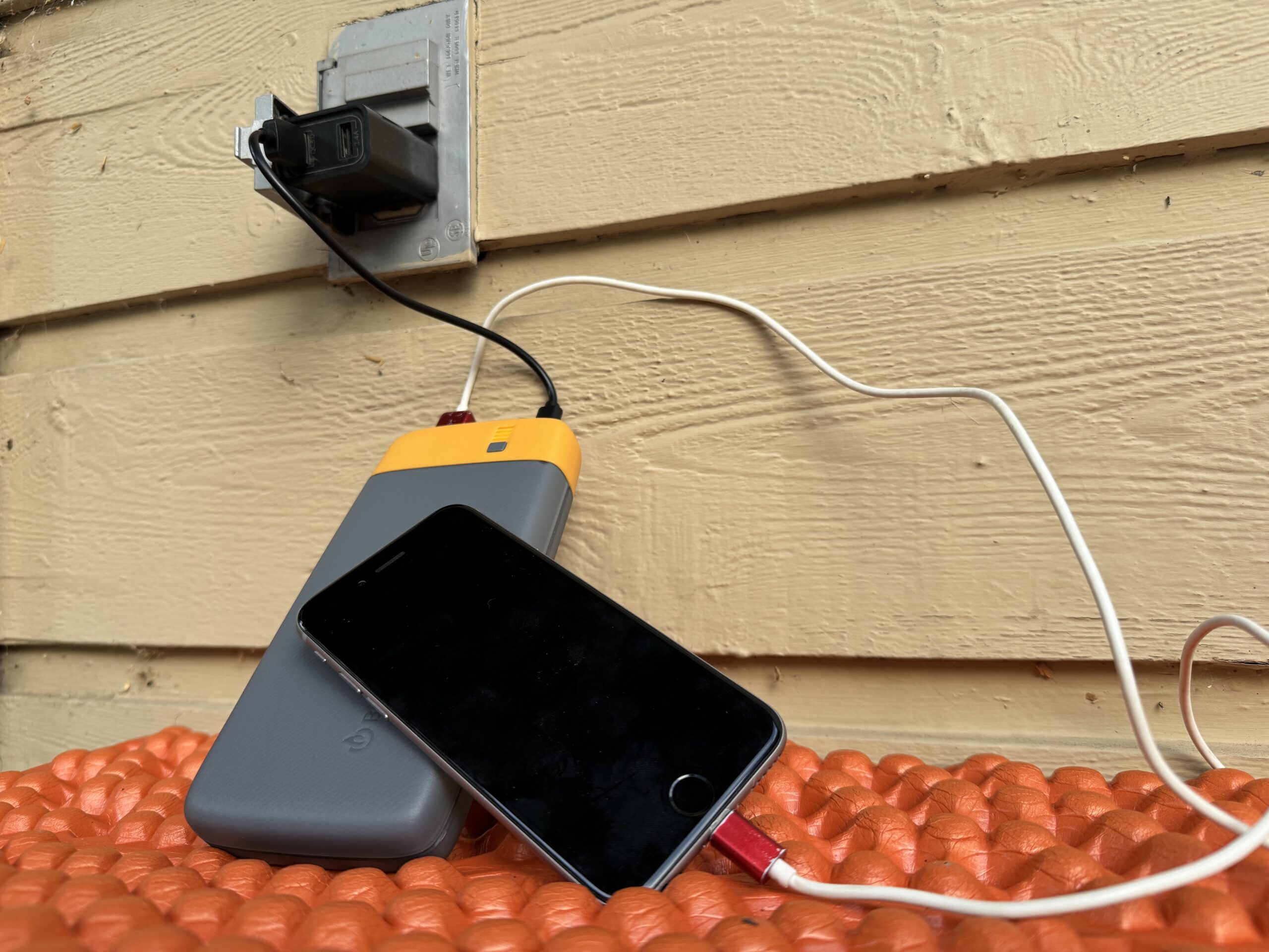 Close up of the BioLite charging from an outlet and a cell phone charging from the power bank simultaneously.