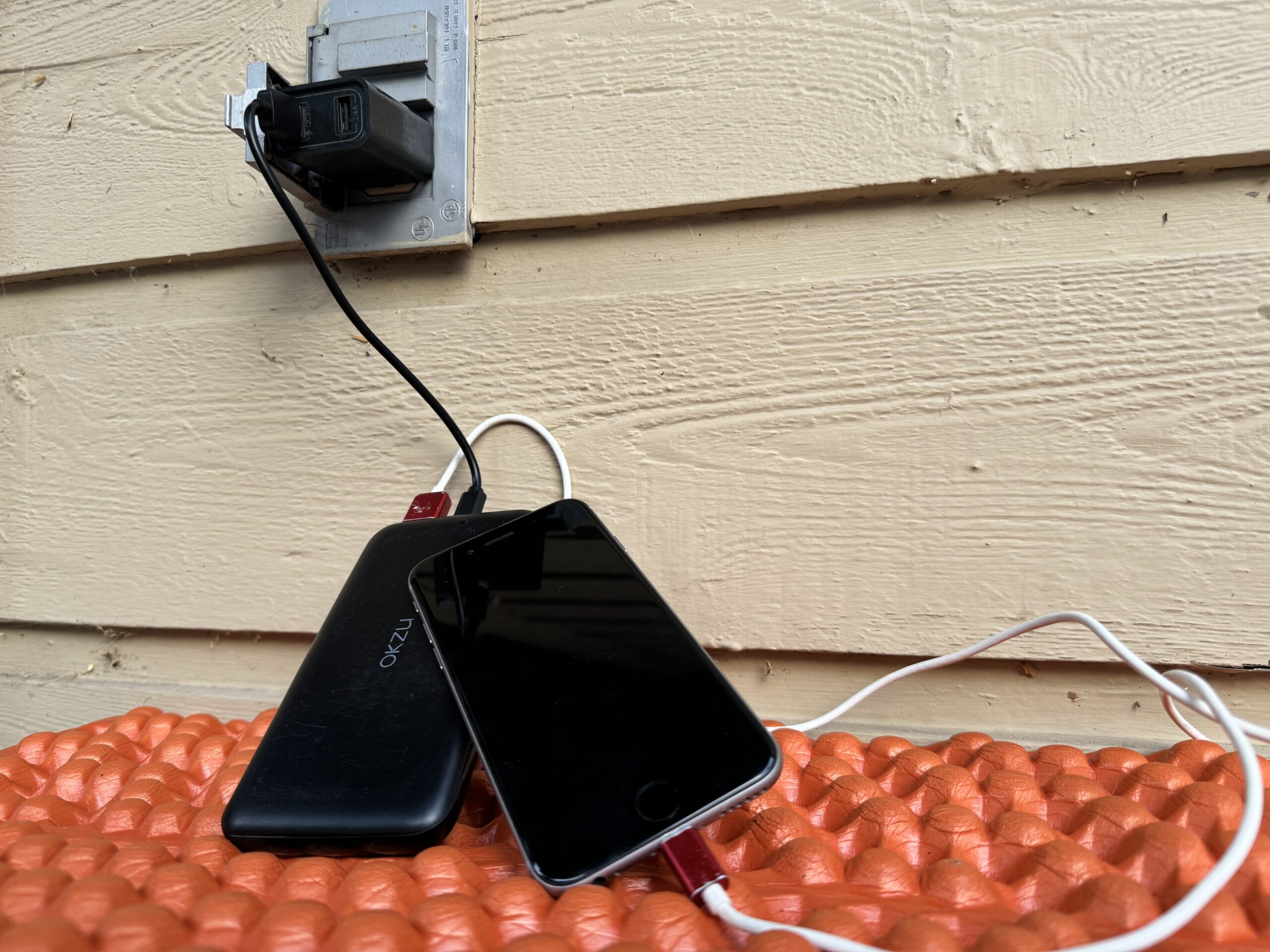 Close up of the OKZU charging from an outlet and a cell phone charging from the power bank simultaneously.