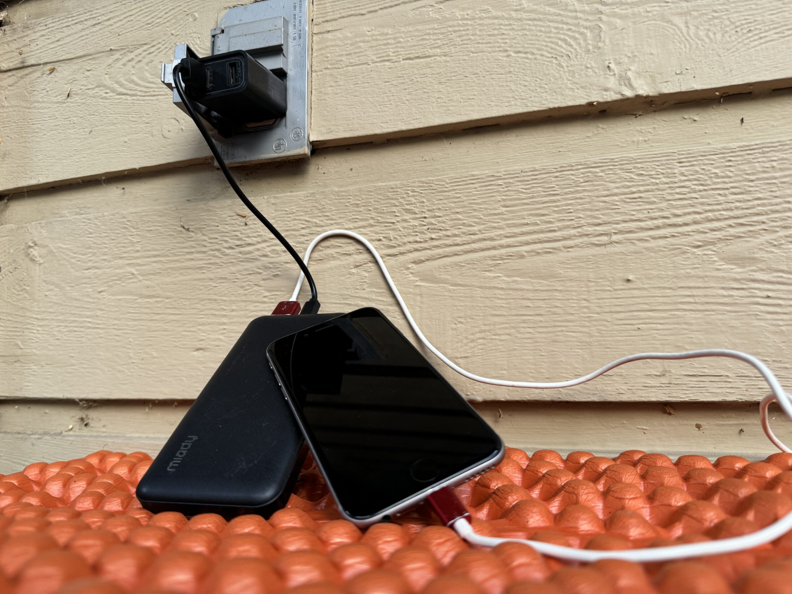 Close up of the Miady charging from an outlet and a cell phone charging from the power bank simultaneously.