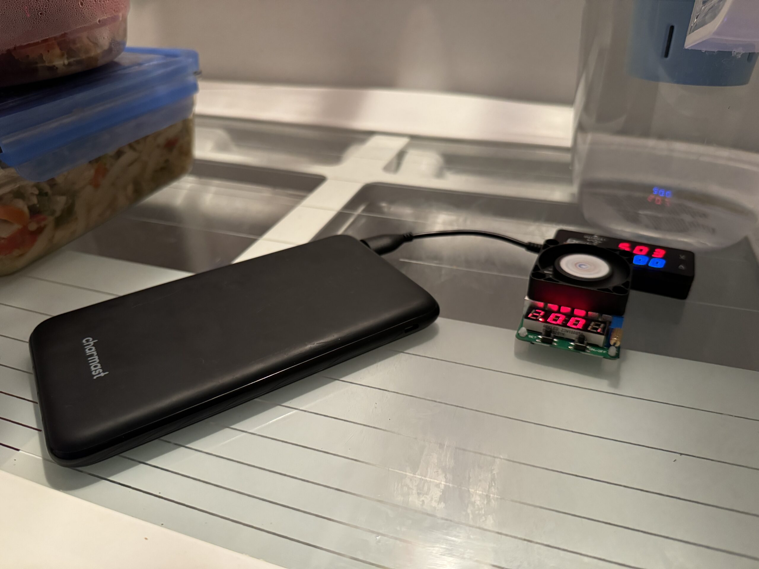 The Charmast power bank is hooked up to a multimeter and dummy resistor load inside a refrigerator with food.