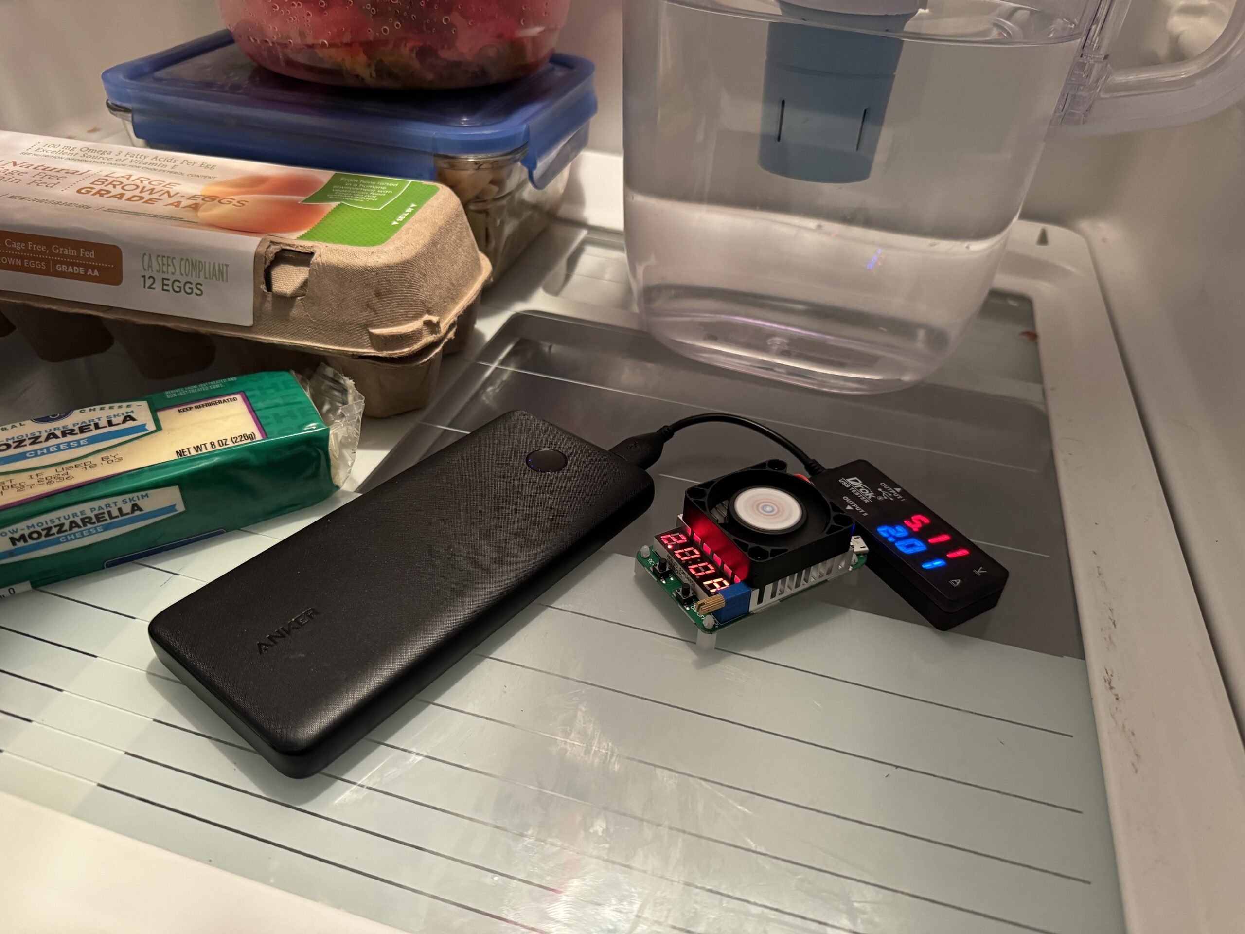 The Anker power bank is hooked up to a multimeter and dummy resistor load inside a refrigerator with food.