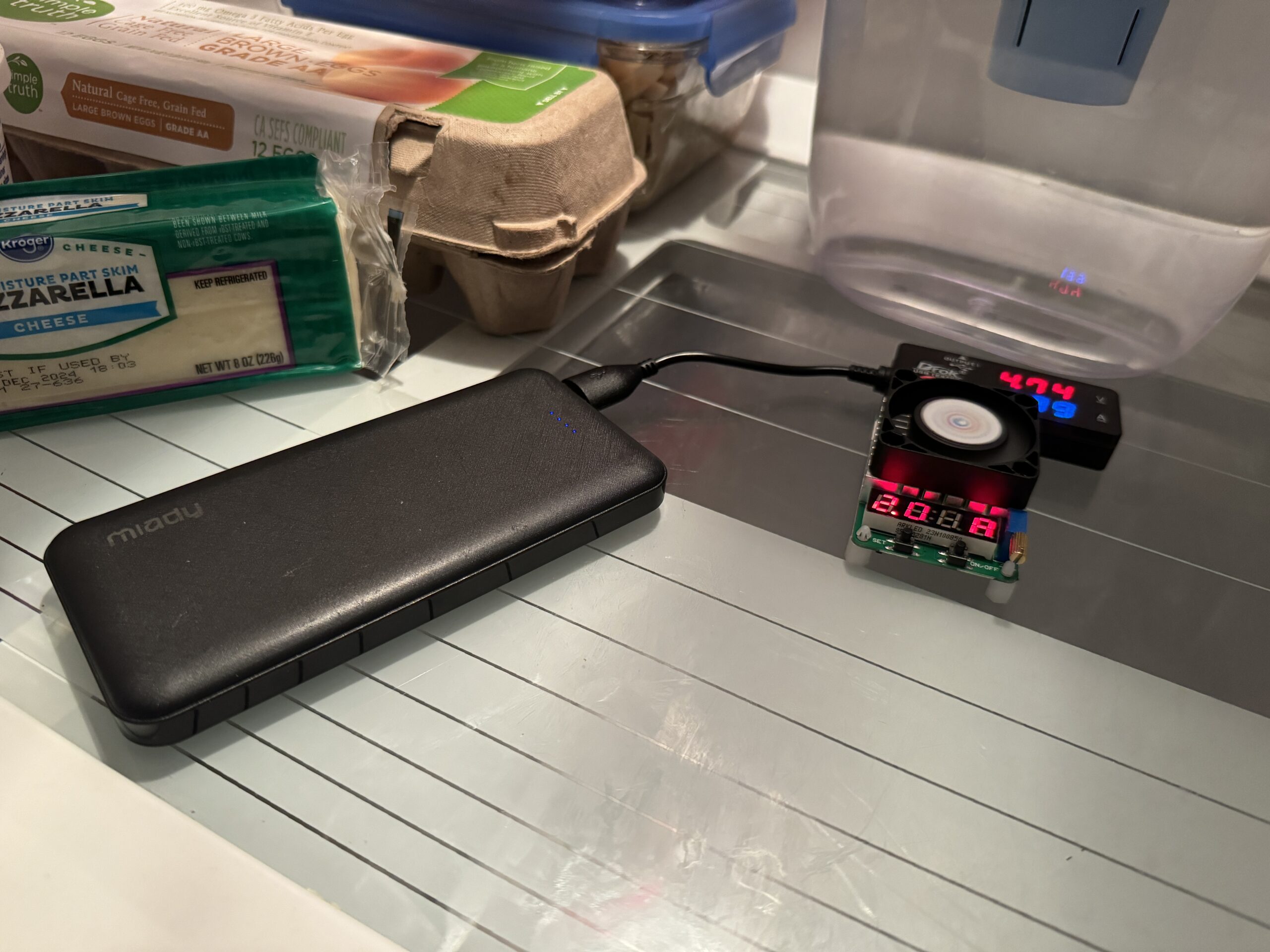 The Miady power bank is hooked up to a multimeter and dummy resistor load inside a refrigerator with food.